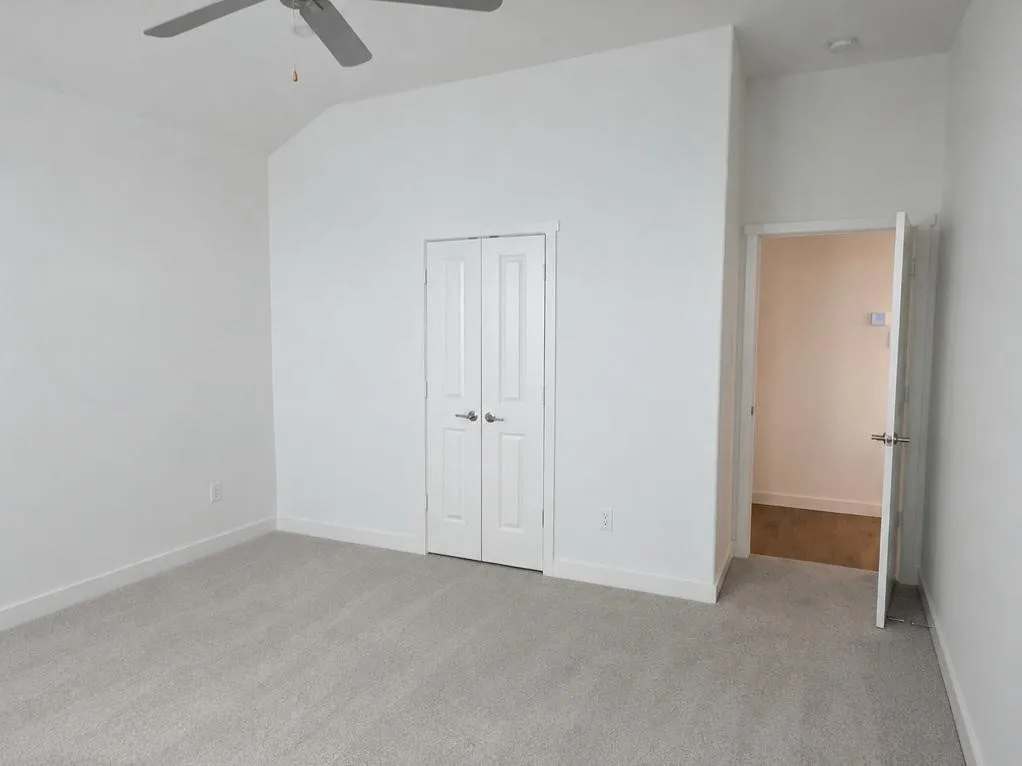 Carpeted room featuring white walls, a vaulted ceiling, and a ceiling fan