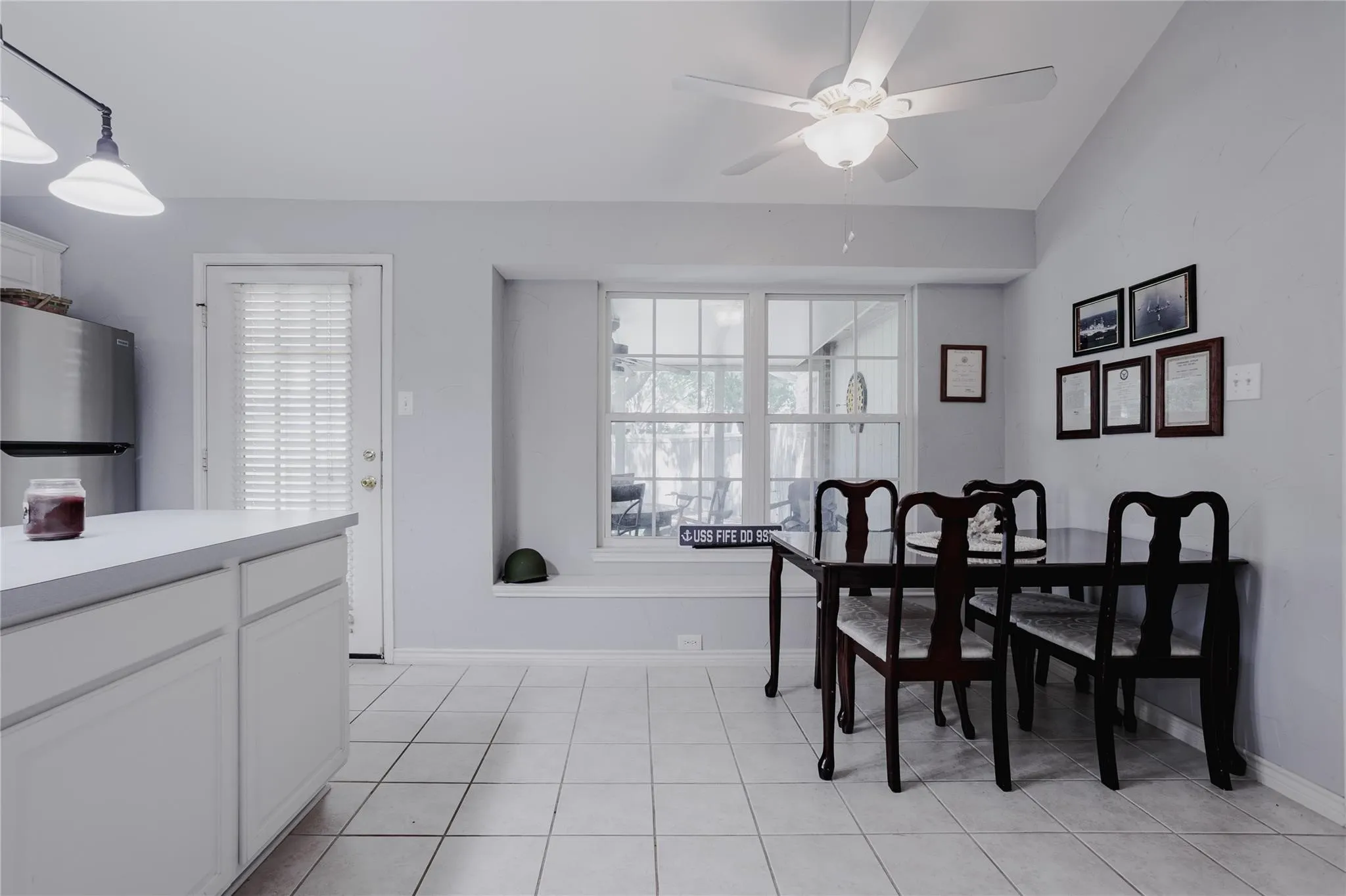 Tile flooring, recessed window, ceiling fan with light fixture, white perimeter cabinetry, stainless steel refrigerator