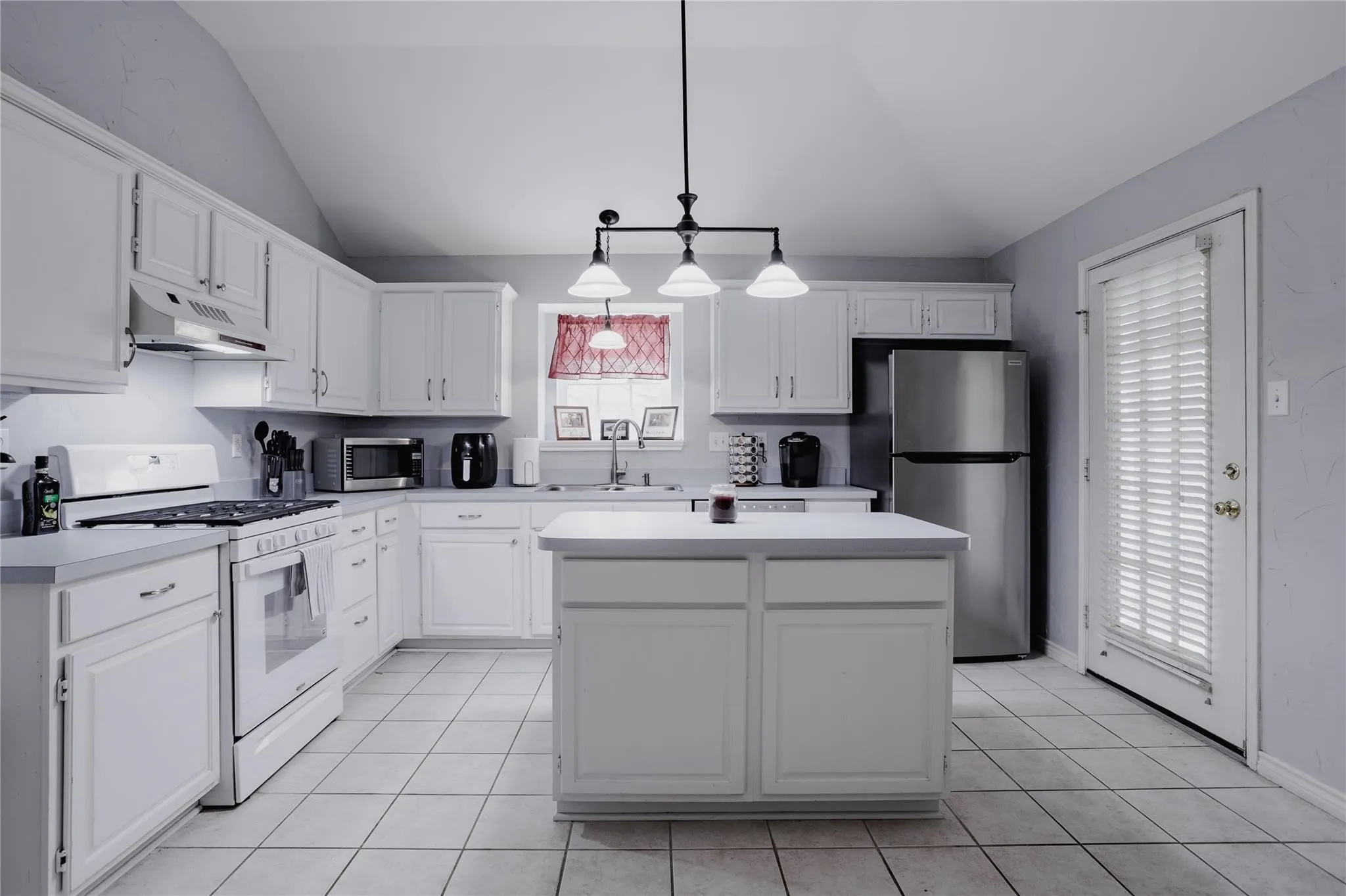Kitchen featuring vaulted ceilings, white cabinetry, a central island, tile flooring, and stainless steel appliances
