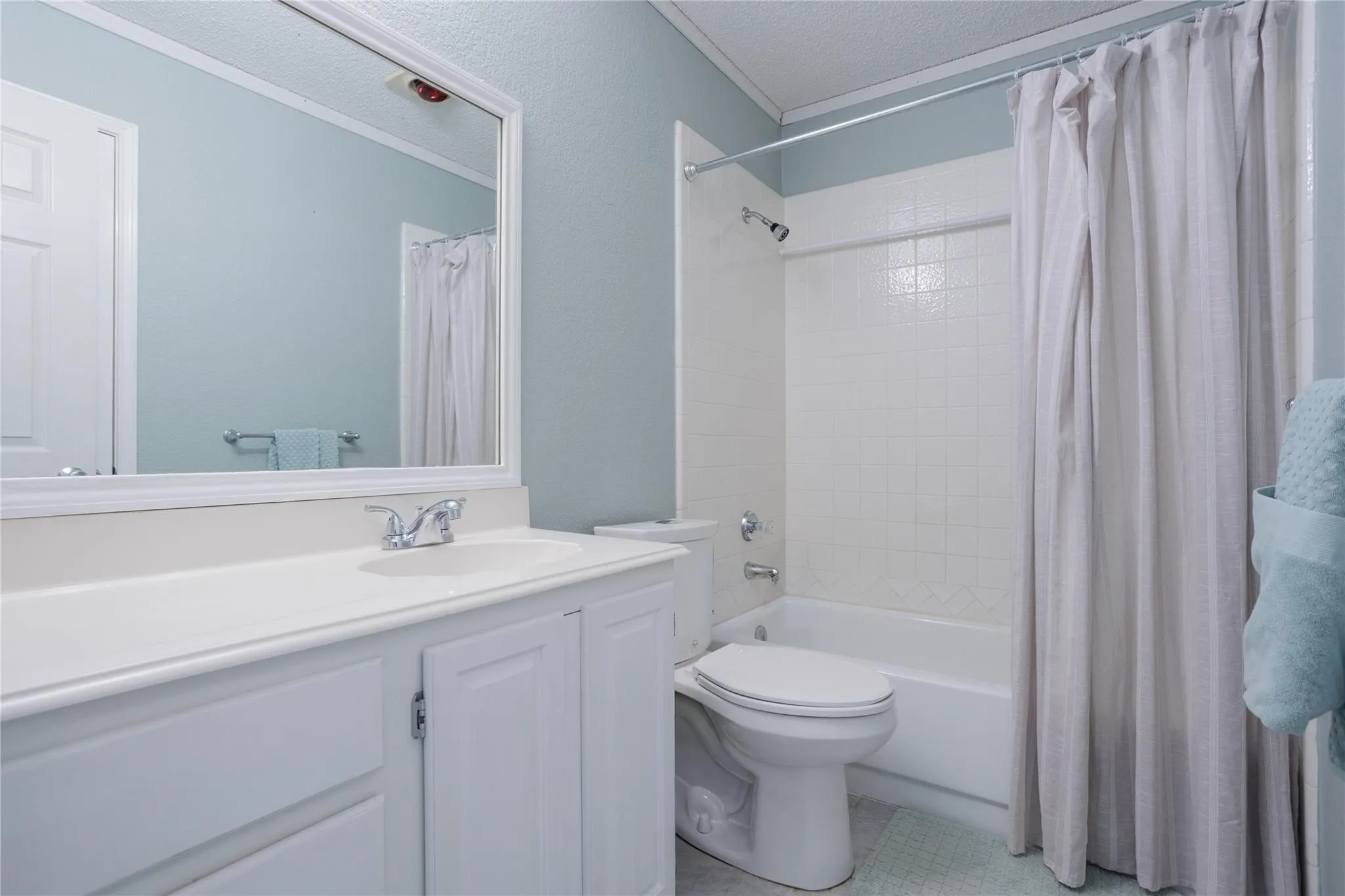 White vanity with integrated sink, chrome faucet, framed mirror, and a shower-over-tub combination with white tile surround
