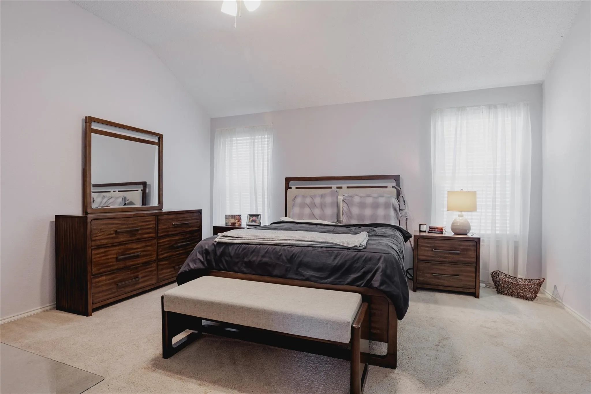 Vaulted ceiling, ceiling fan, two windows with white blinds, and light-toned carpet flooring
