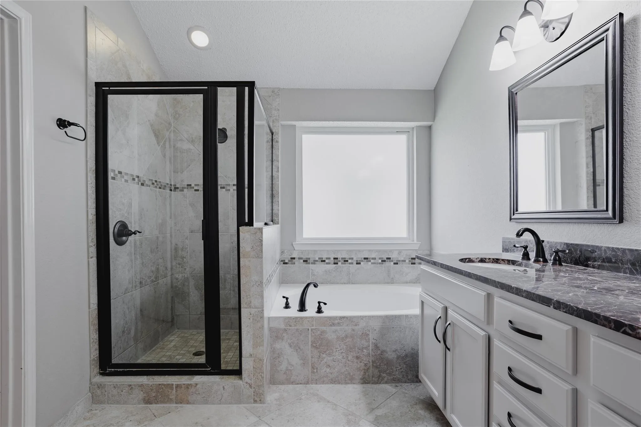 Walk-in shower with dark-framed glass enclosure, built-in soaking tub, vanity with stone countertop, under-mount sink, and dark-finish hardware