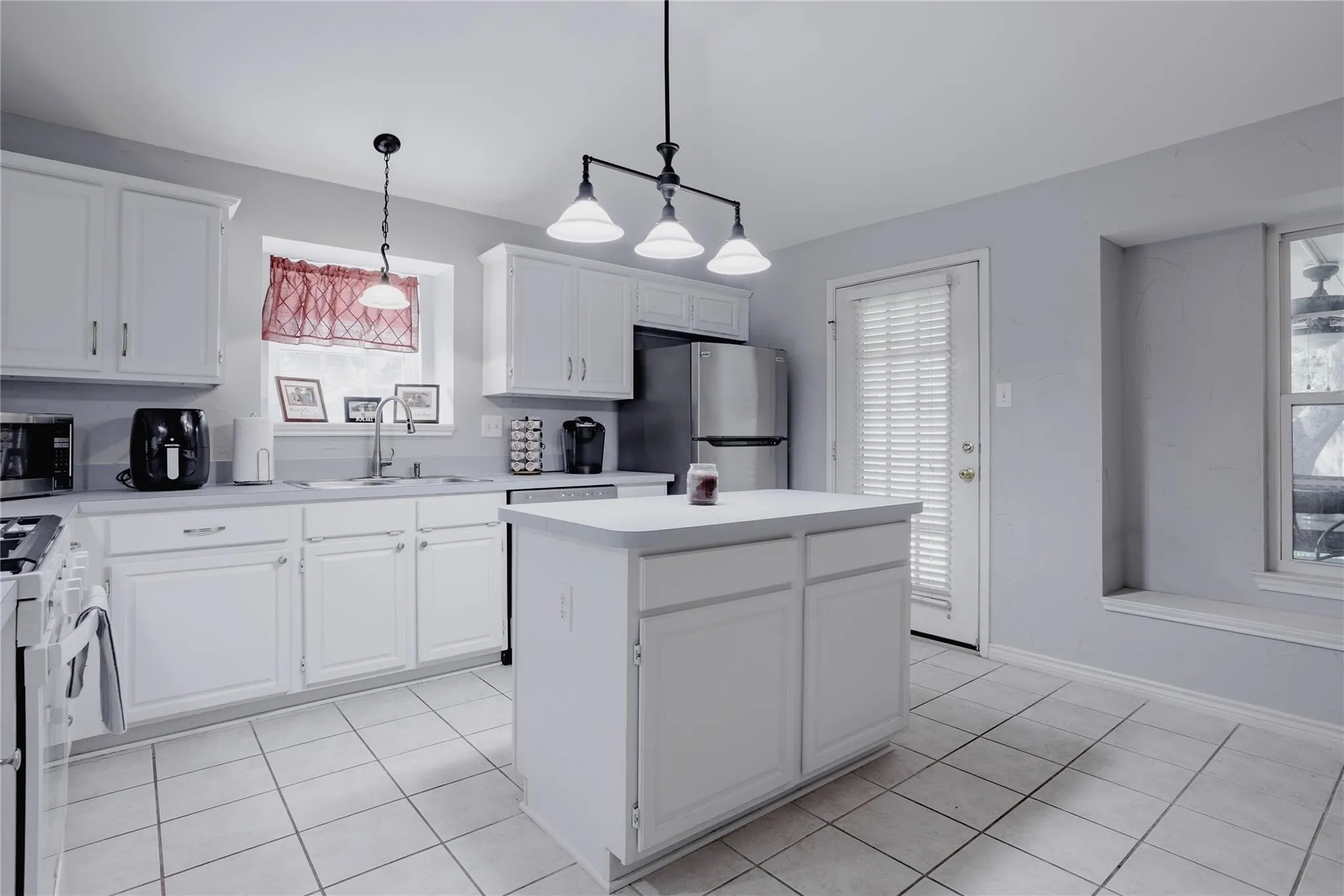 White cabinetry, tile flooring, central island, stainless steel refrigerator, and recessed window