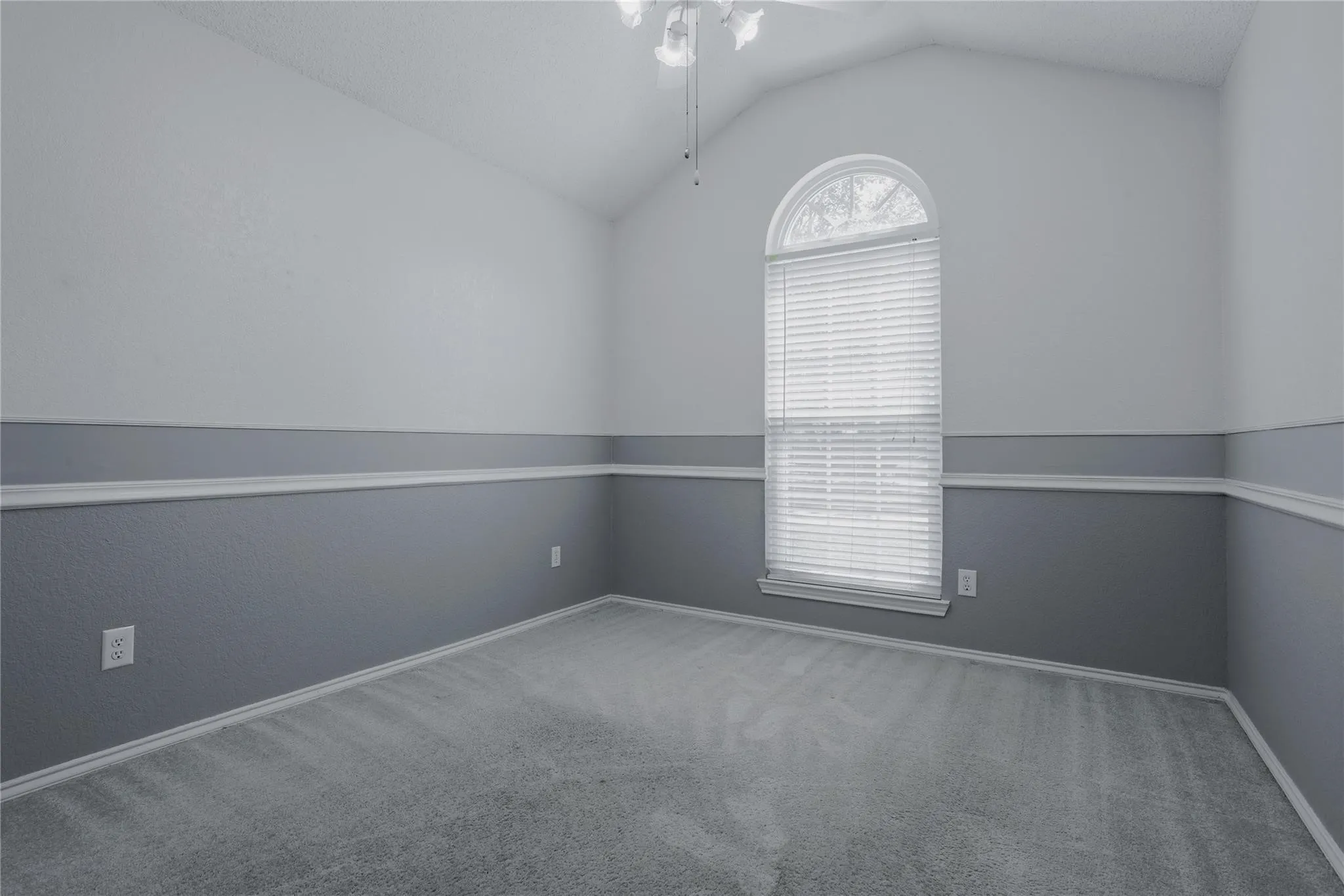 Vaulted ceiling with a ceiling fan, arched window with blinds, two-tone wall treatment, decorative chair rail molding, and soft carpeting