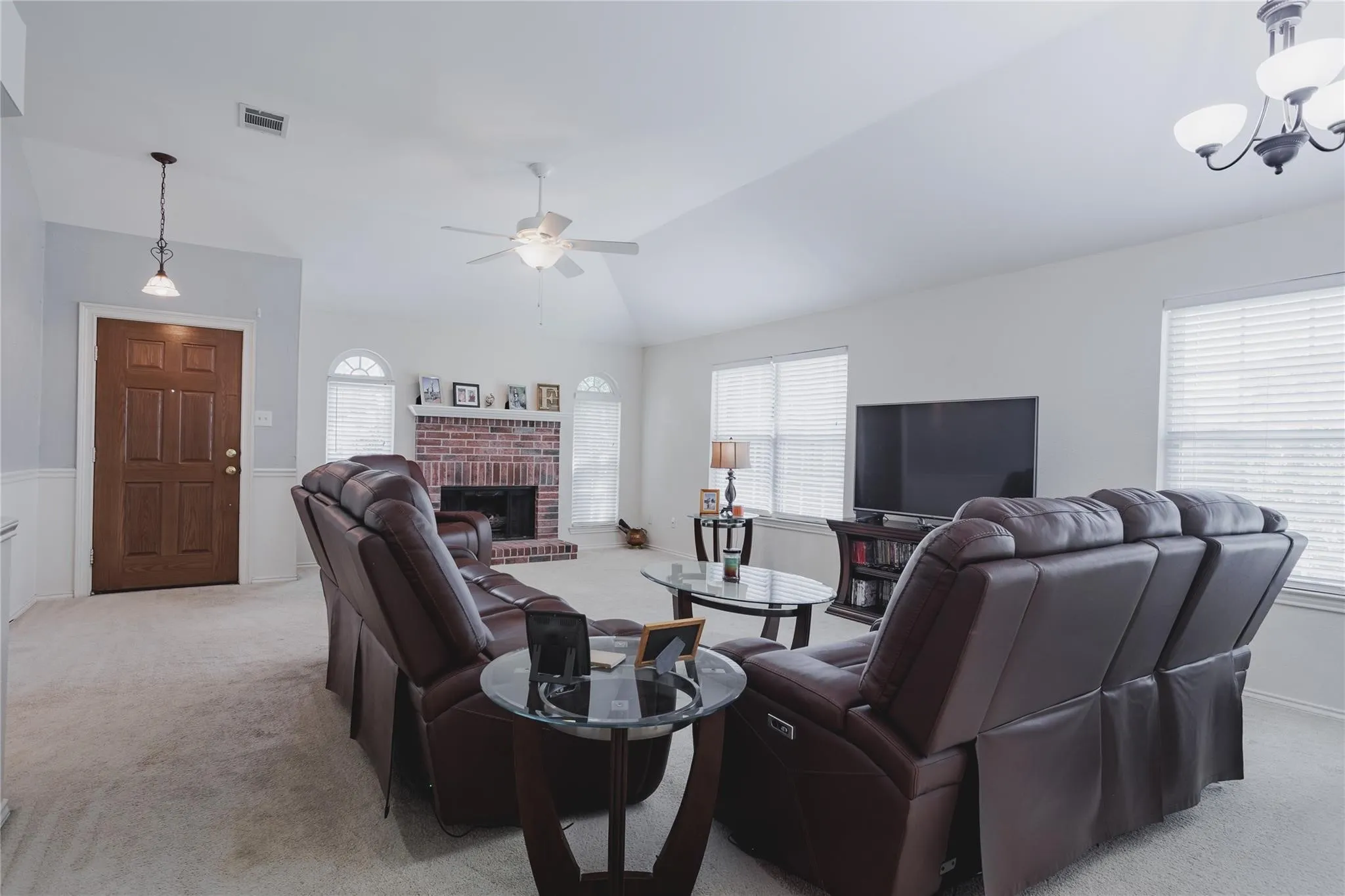 Vaulted ceiling with ceiling fan, brick fireplace, arched windows, and a panel front door