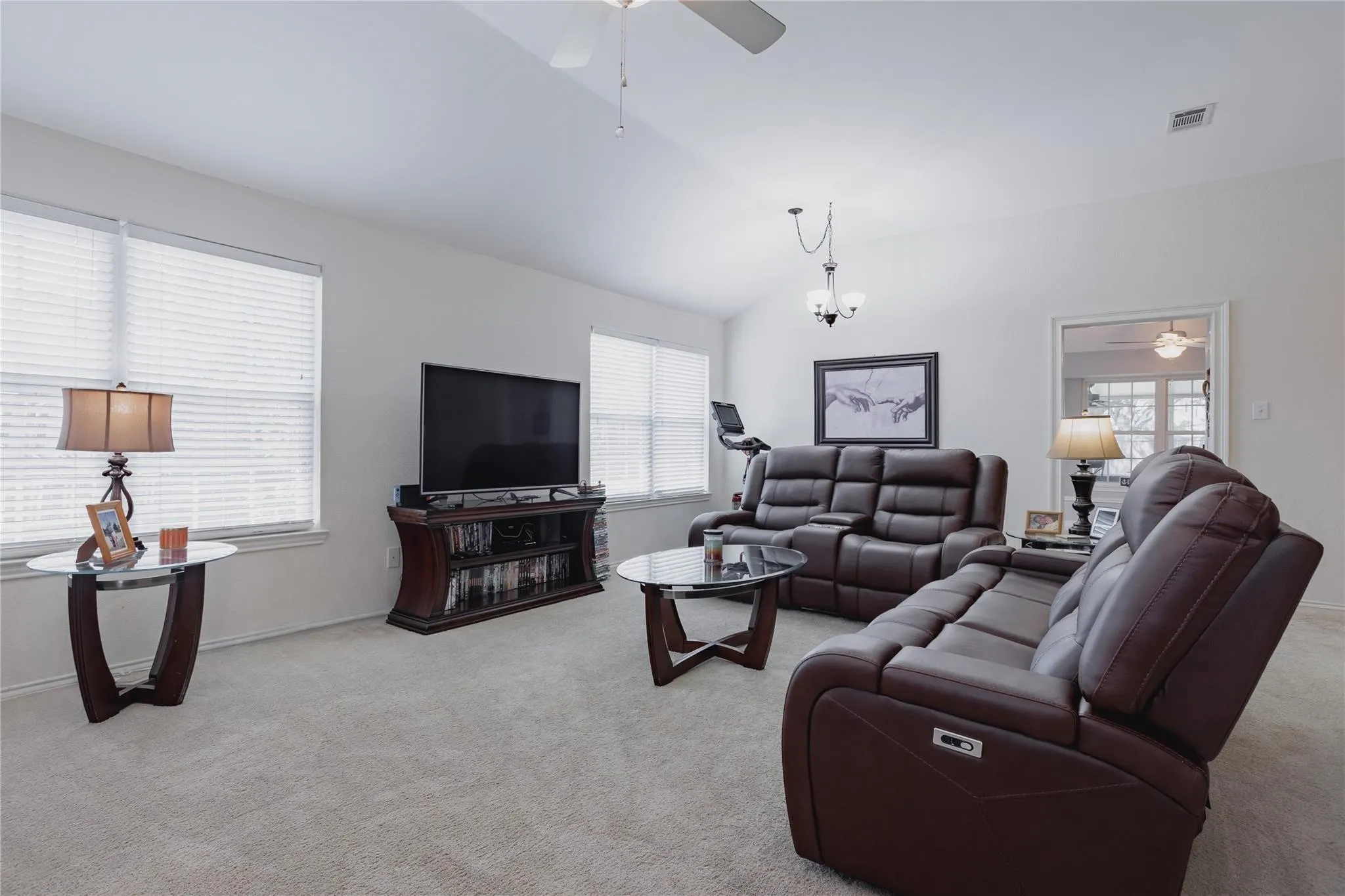 Vaulted ceiling with a ceiling fan, neutral carpet flooring, and multiple windows