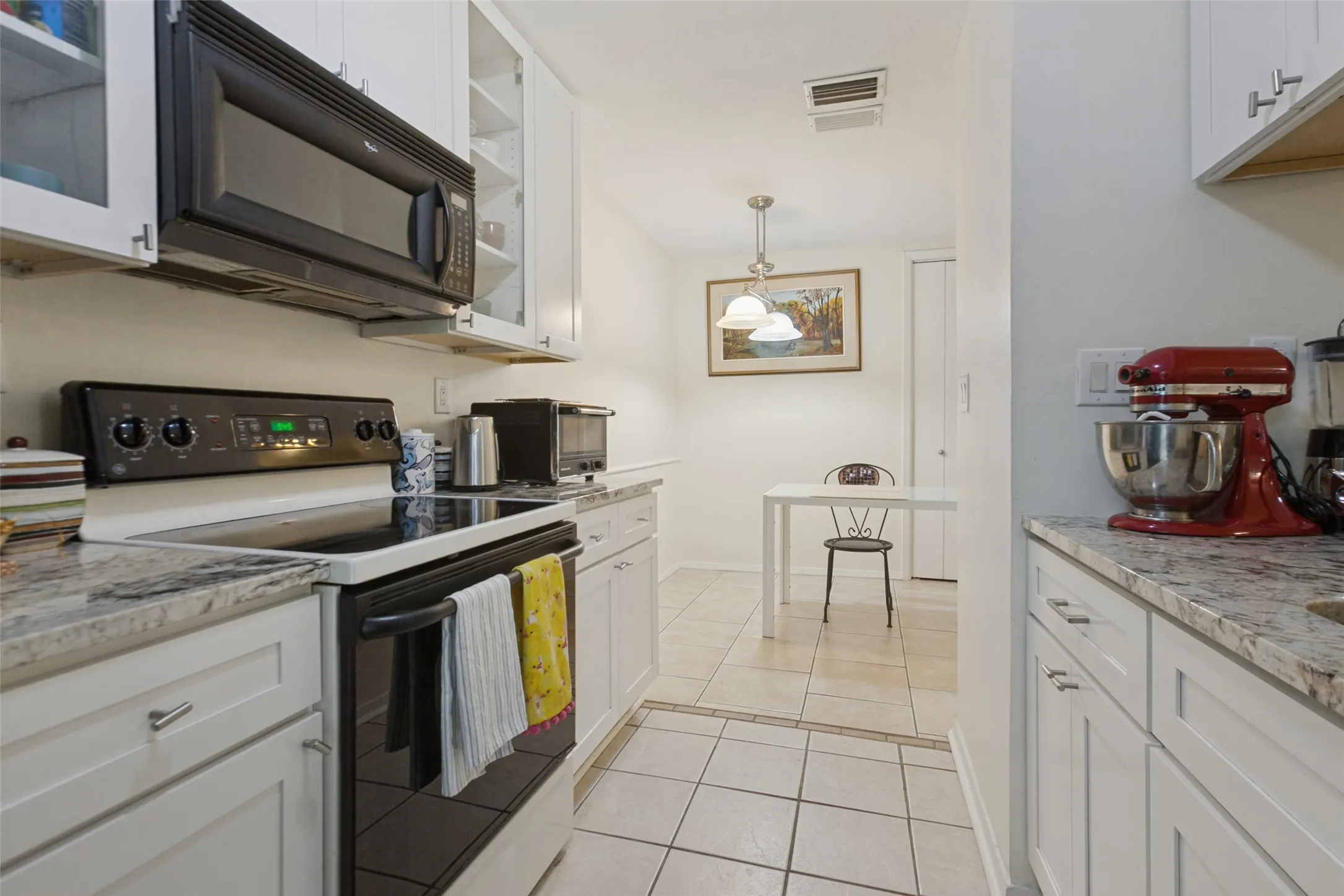 White cabinetry with brushed nickel hardware, light-toned stone-finish countertops, black built-in microwave, black electric range, and light-toned floor tiling
