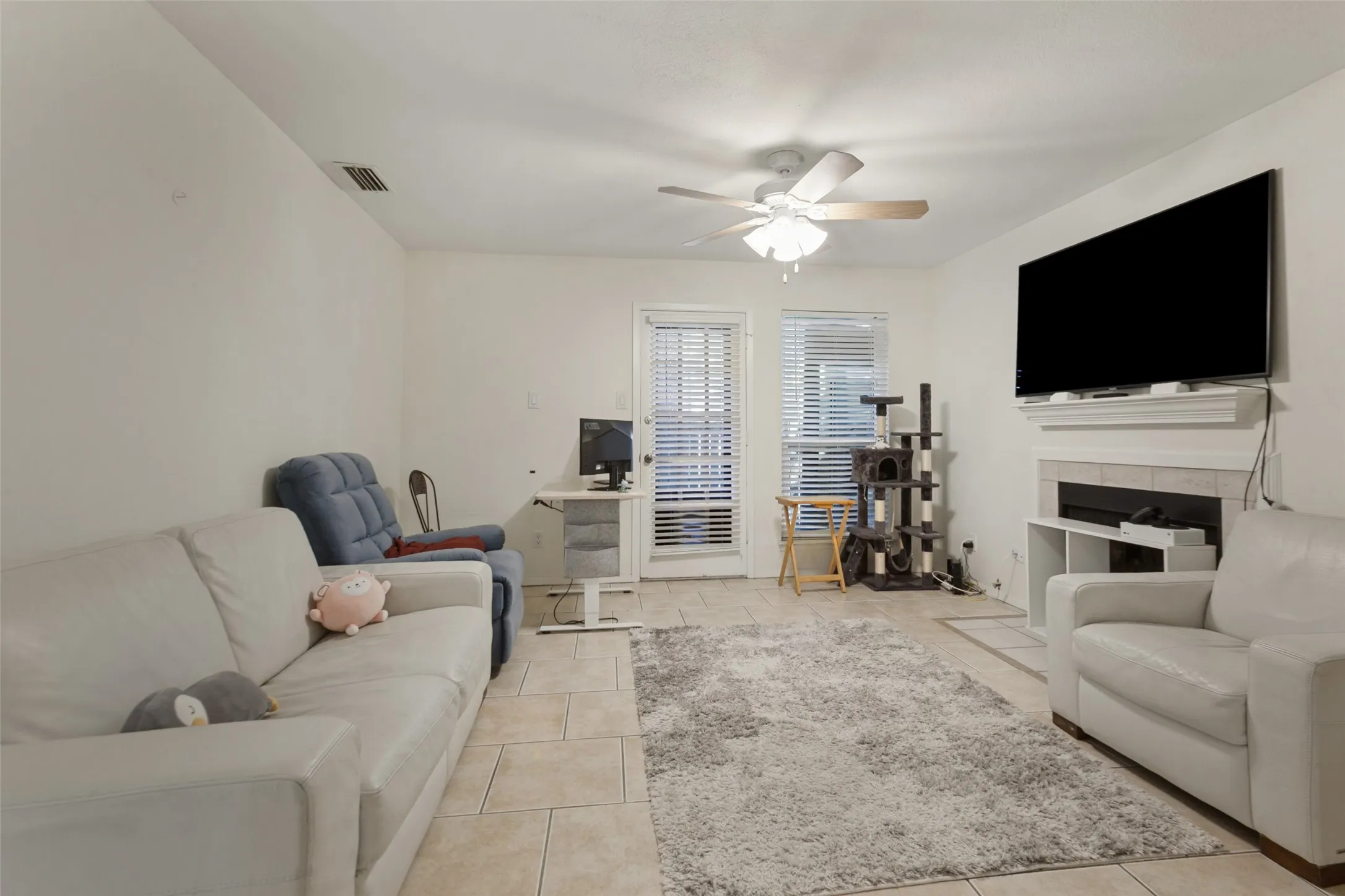 Tile flooring, recessed fireplace with mantle, ceiling fan, and two windows with blinds