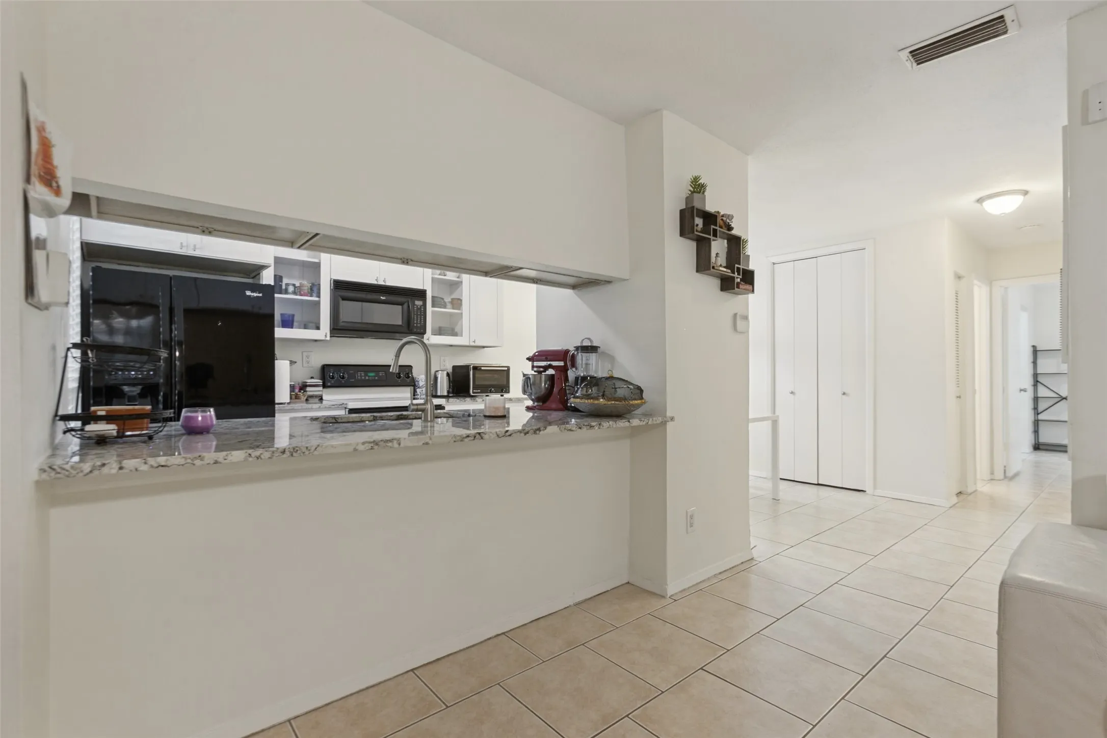 Kitchen pass-through with a stone-finish countertop, white cabinetry, and stainless-steel finish faucet