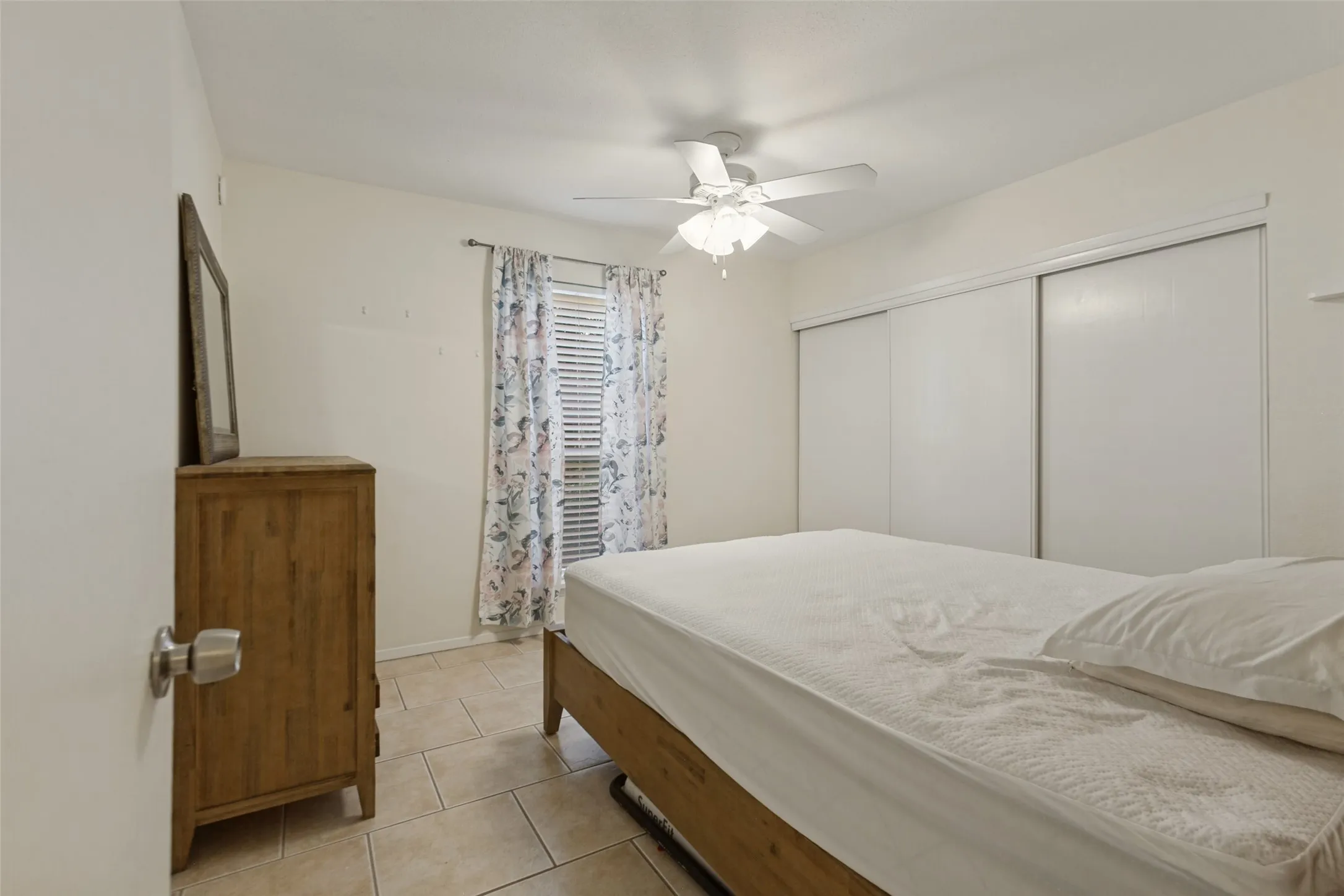 Tile flooring, window with blinds, ceiling fan with light fixture, and sliding closet doors