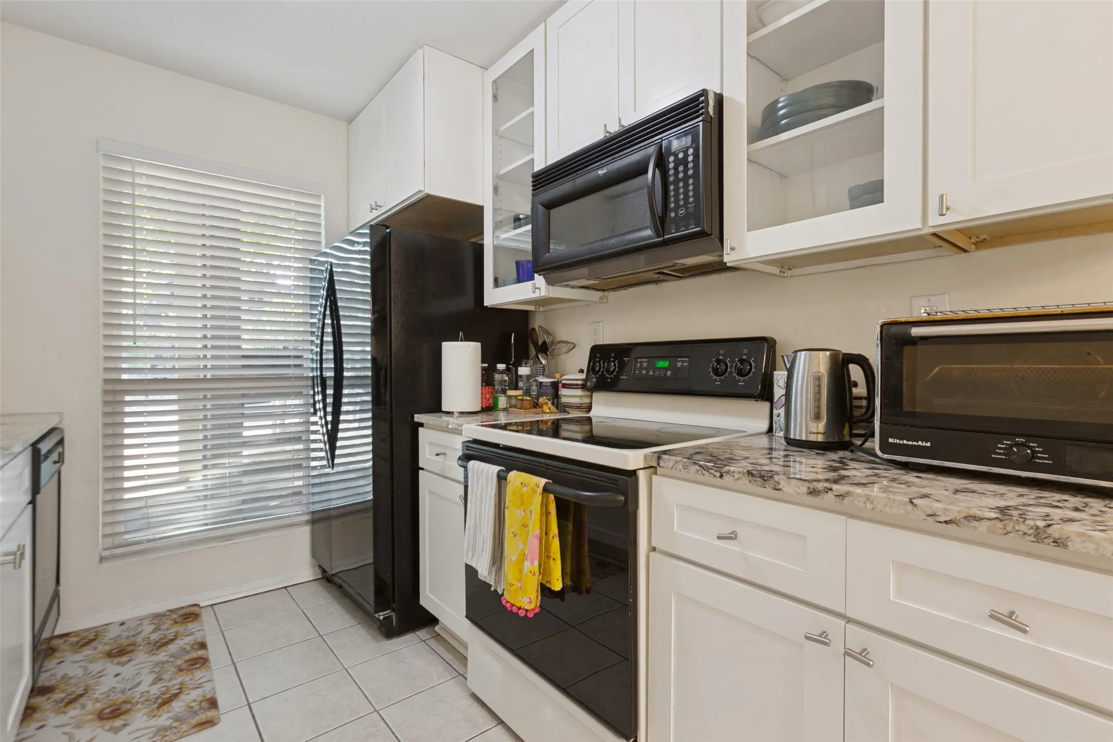 White shaker-style cabinetry with varied glass-front upper cabinets, light-toned countertops, and a full suite of black appliances