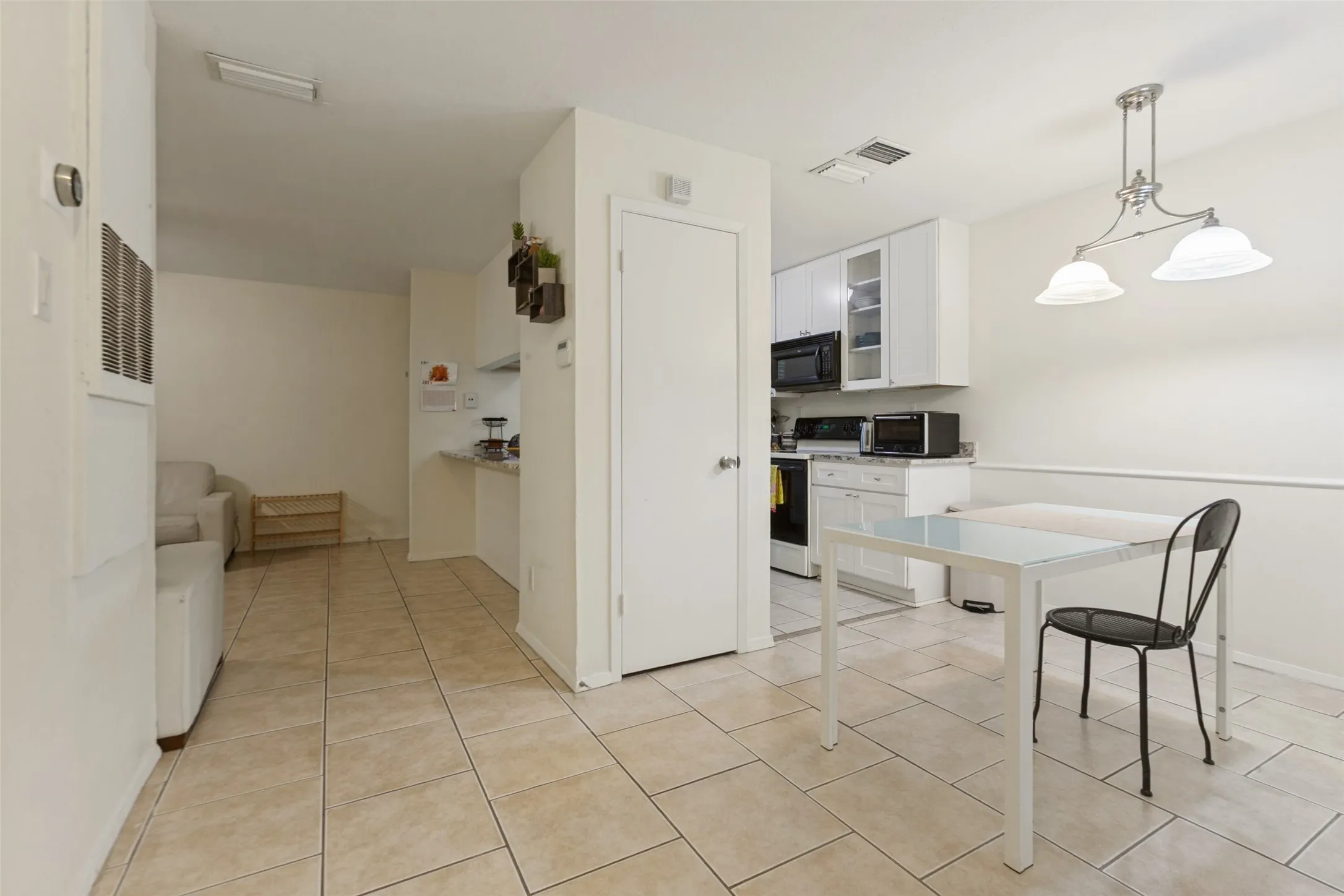 Kitchen featuring white cabinetry with upper glass-front display cabinets, black appliances, and a dining area with a two-light pendant fixture