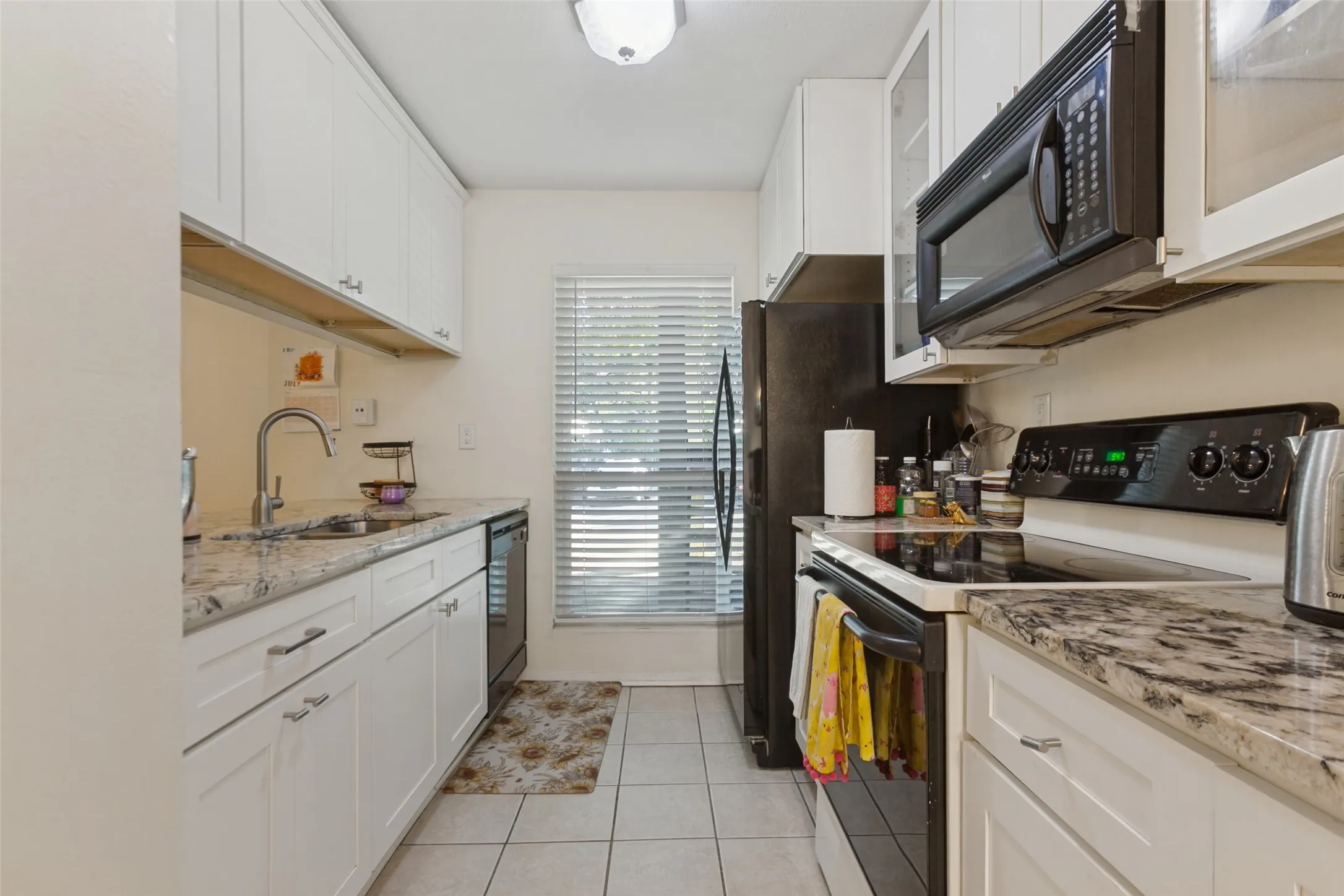 White shaker-style cabinetry, light-toned countertops, tile flooring, and integrated appliances