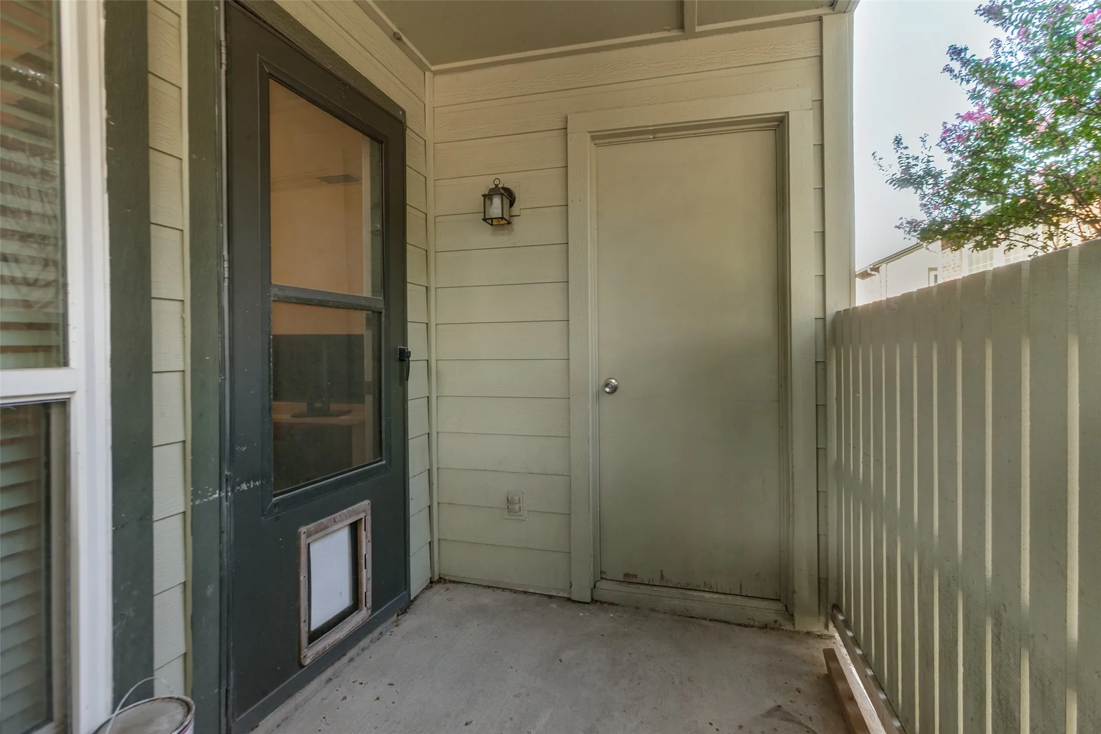 Enclosed patio with concrete flooring, louvered siding, a built-in outdoor light fixture, and an exterior storage door
