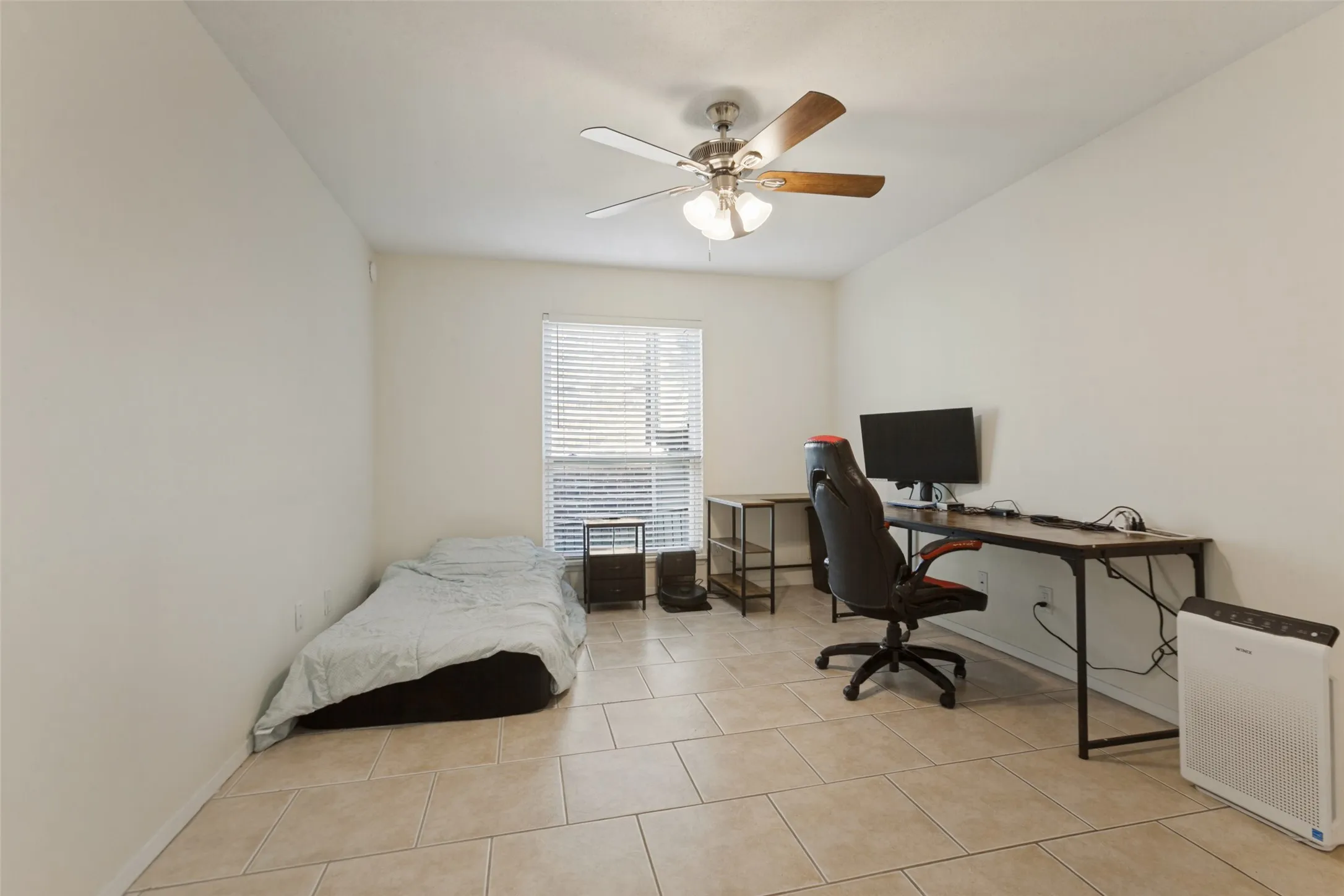 Neutral-toned tile flooring, white walls, a window with blinds, and a ceiling fan with light fixture