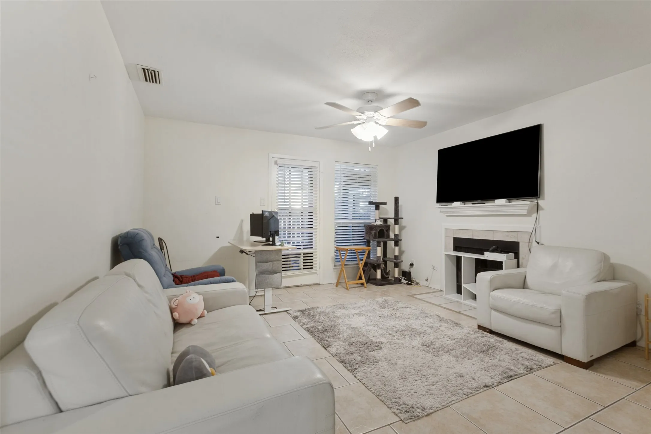 Living area with tile flooring, a built-in fireplace, ceiling fan, and window with blinds