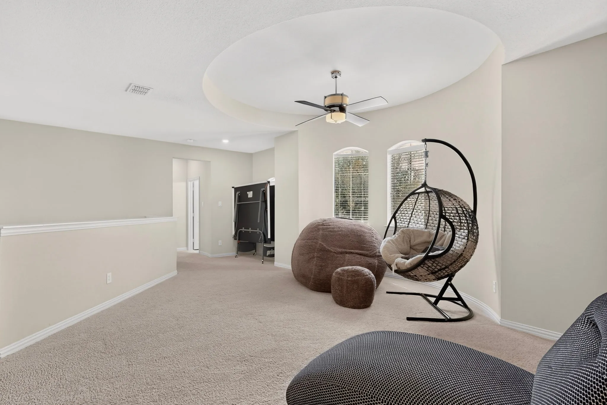 Carpeted room featuring a circular tray ceiling, ceiling fan, and two arched windows