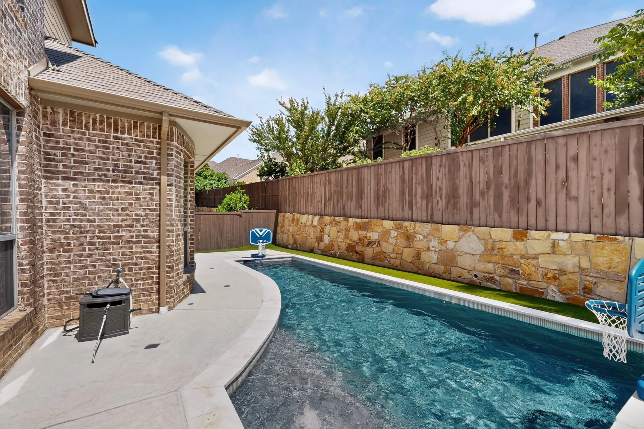 Brick exterior, curved concrete patio, in-ground swimming pool, stone retaining wall, and wood privacy fencing