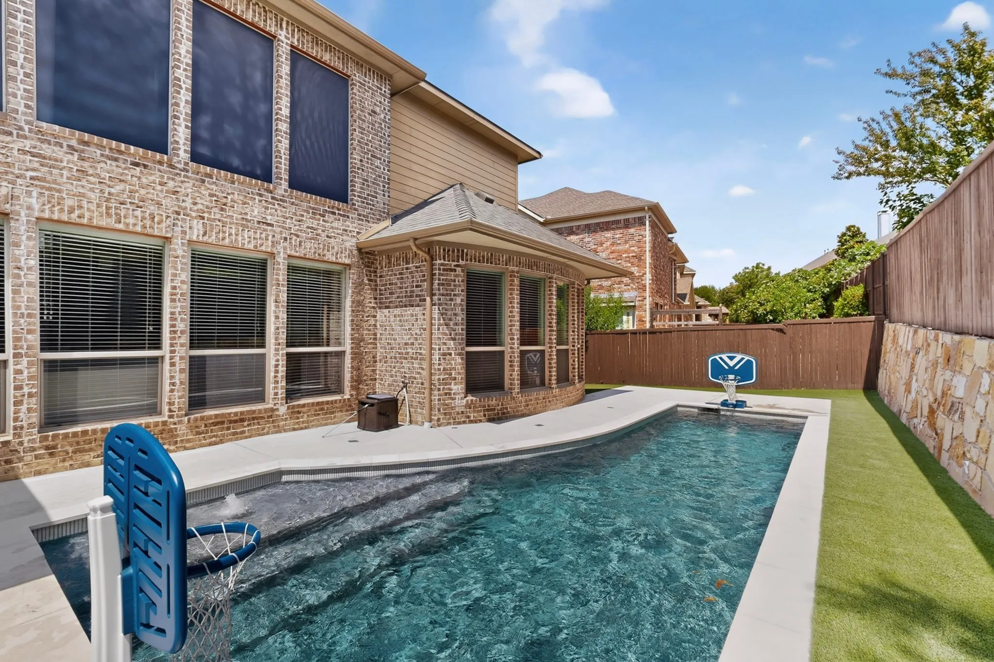 Brick exterior with multiple windows, inground pool with integrated steps, artificial turf area, and a stone retaining wall