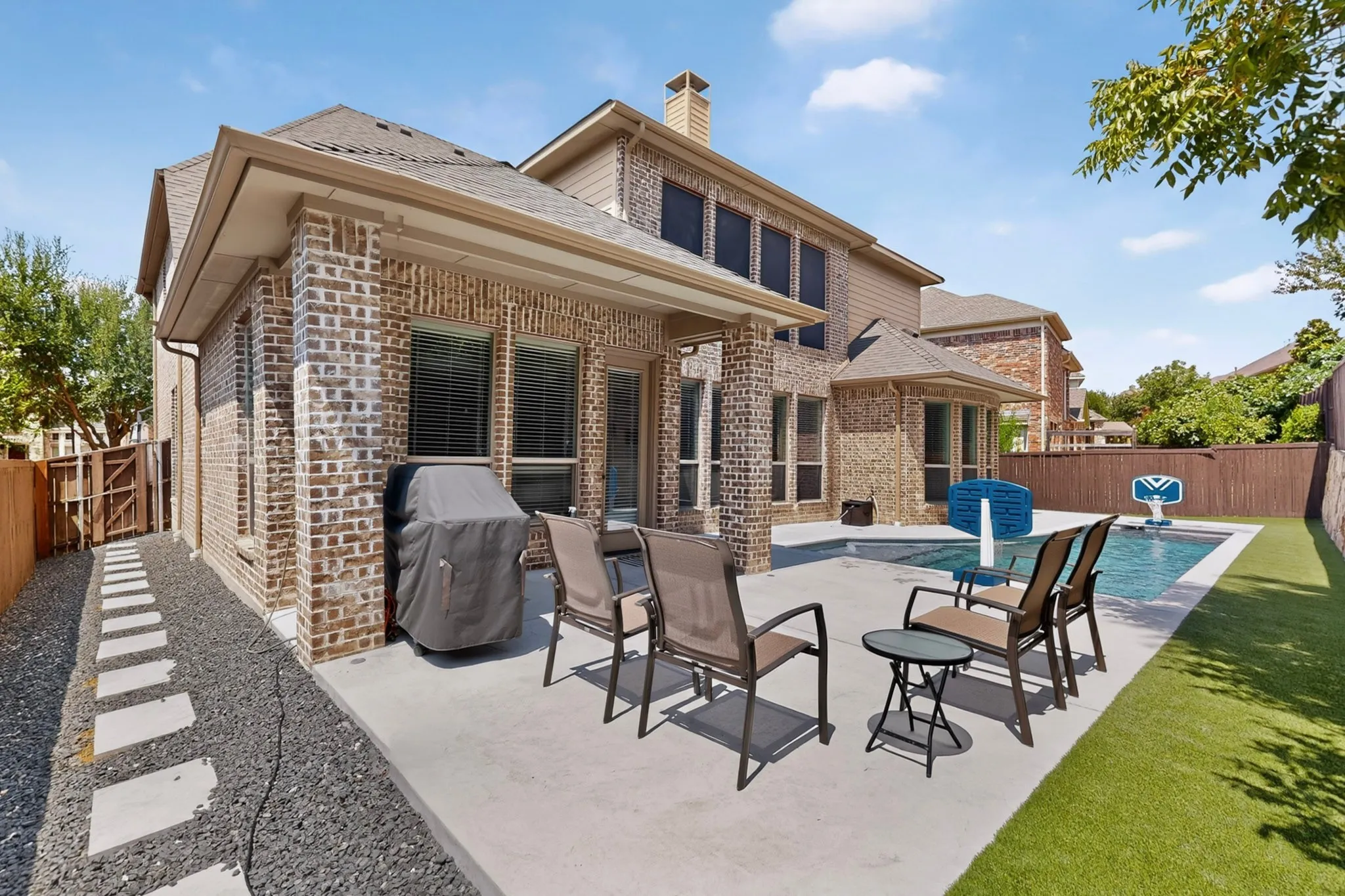 Brick exterior with an expansive concrete patio, a private swimming pool, and artificial turf