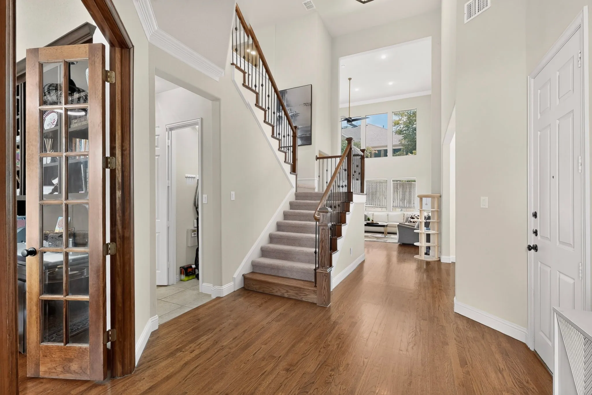 Two-story entryway with wood-finish flooring, a carpeted staircase with wood and wrought iron railing, and a multi-pane front door