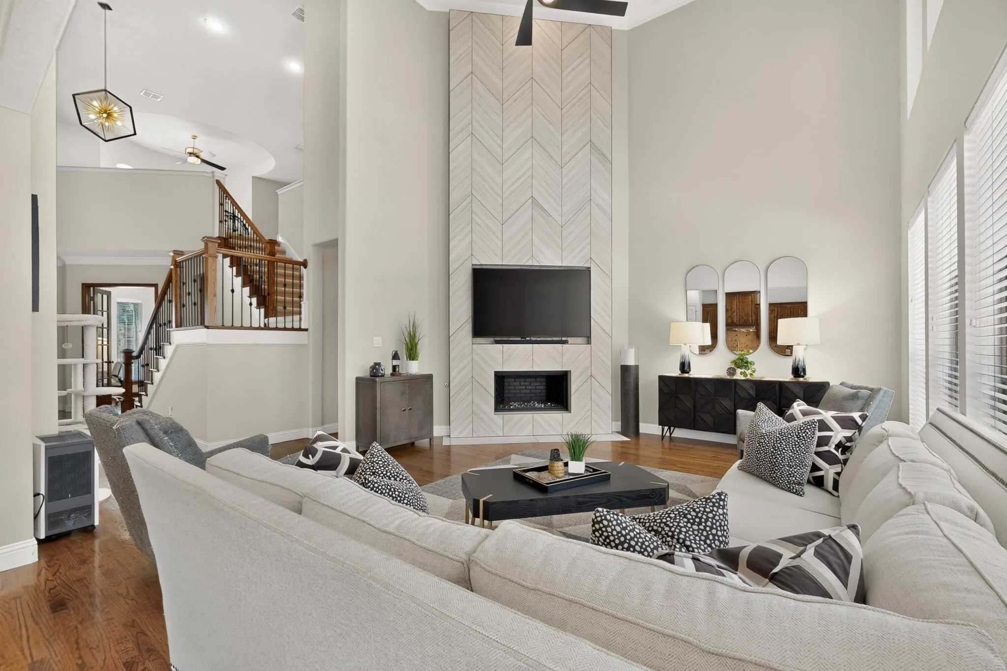 Two-story living area with a chevron-patterned fireplace surround, built-in electric fireplace, and a light-toned ceiling fan