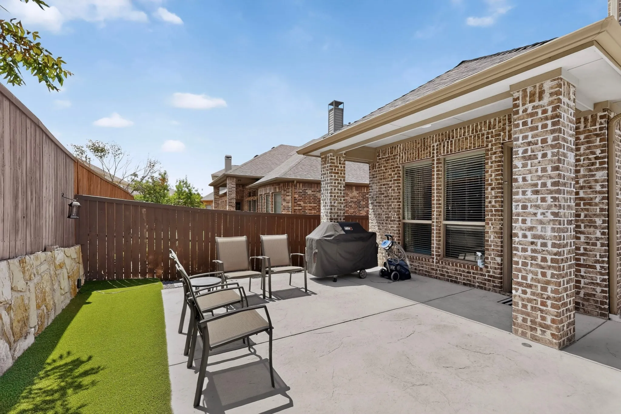 Outdoor living space featuring a concrete patio, artificial turf, and a stone retaining wall