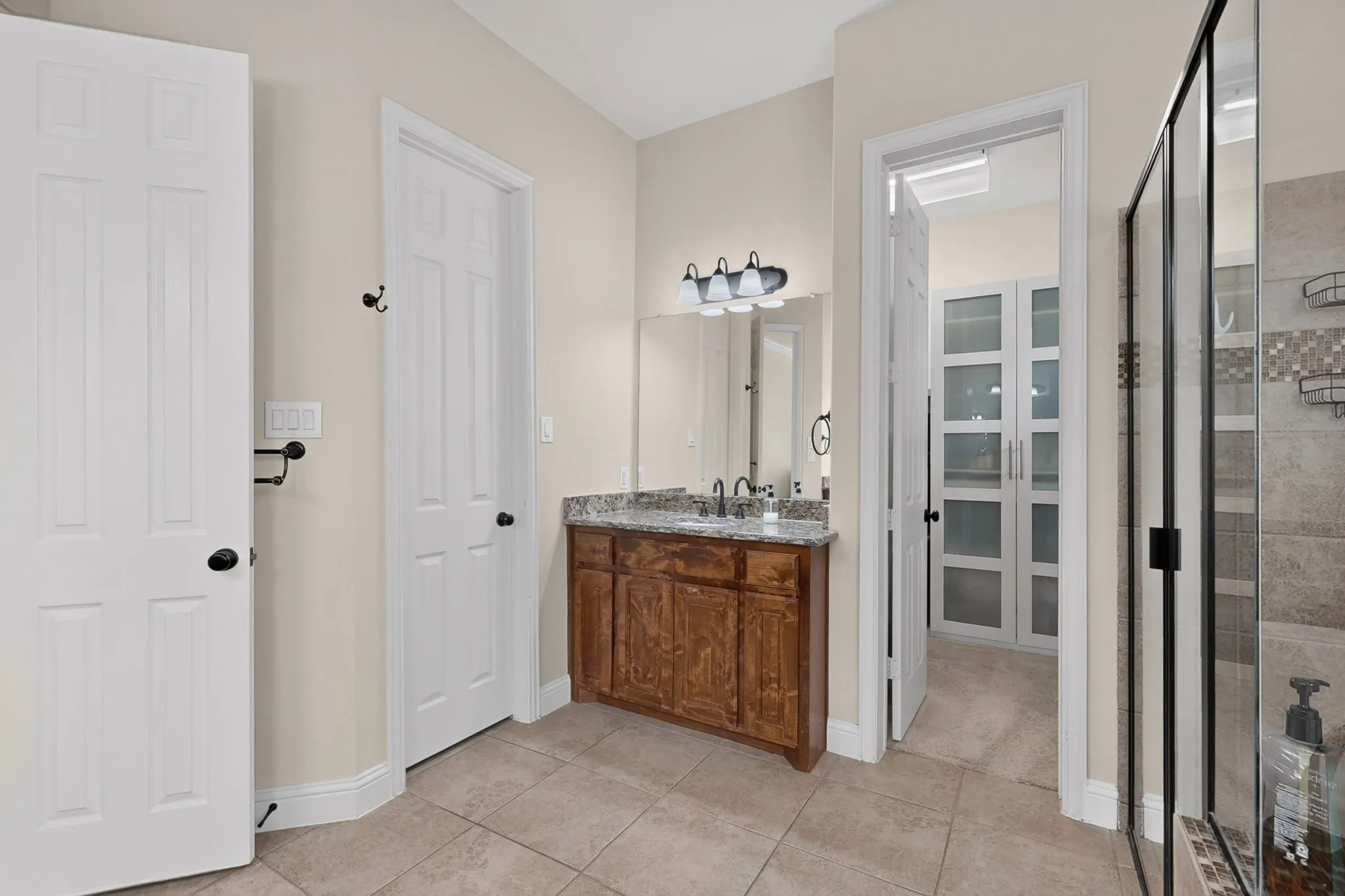 Wood-finish vanity with a stone countertop, tile flooring, and a glass-enclosed shower with tiled walls