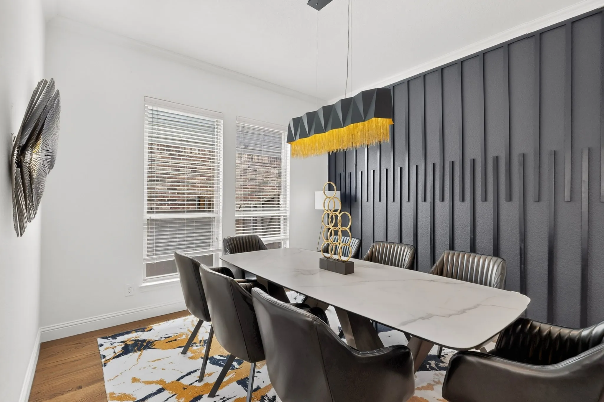 Accent wall with vertical paneling, multiple windows with blinds, wood-finish flooring, and a contemporary chandelier
