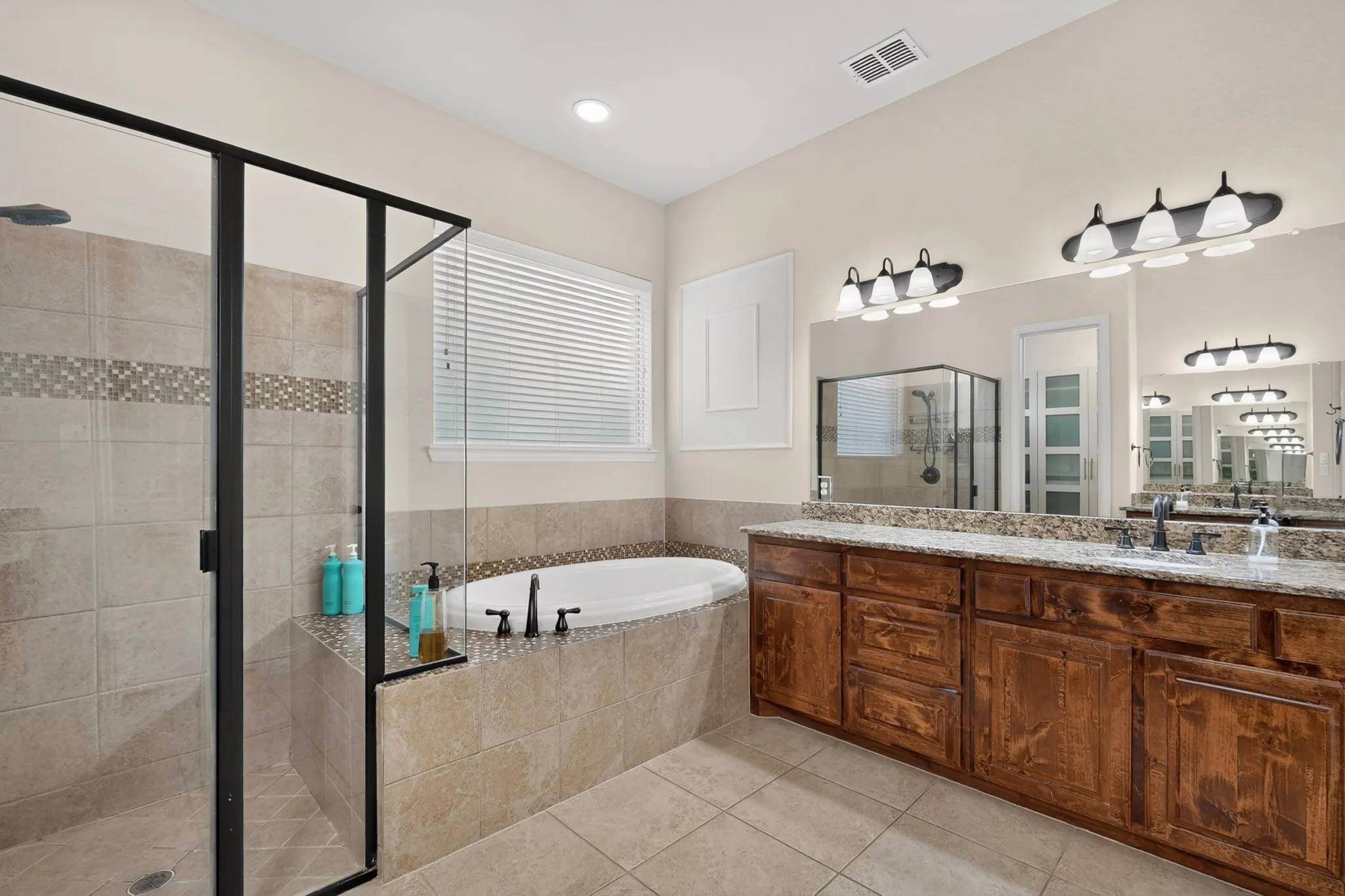 Enclosed shower with black-framed glass, built-in soaking tub, wood-finish vanity with dual sinks, and granite countertops