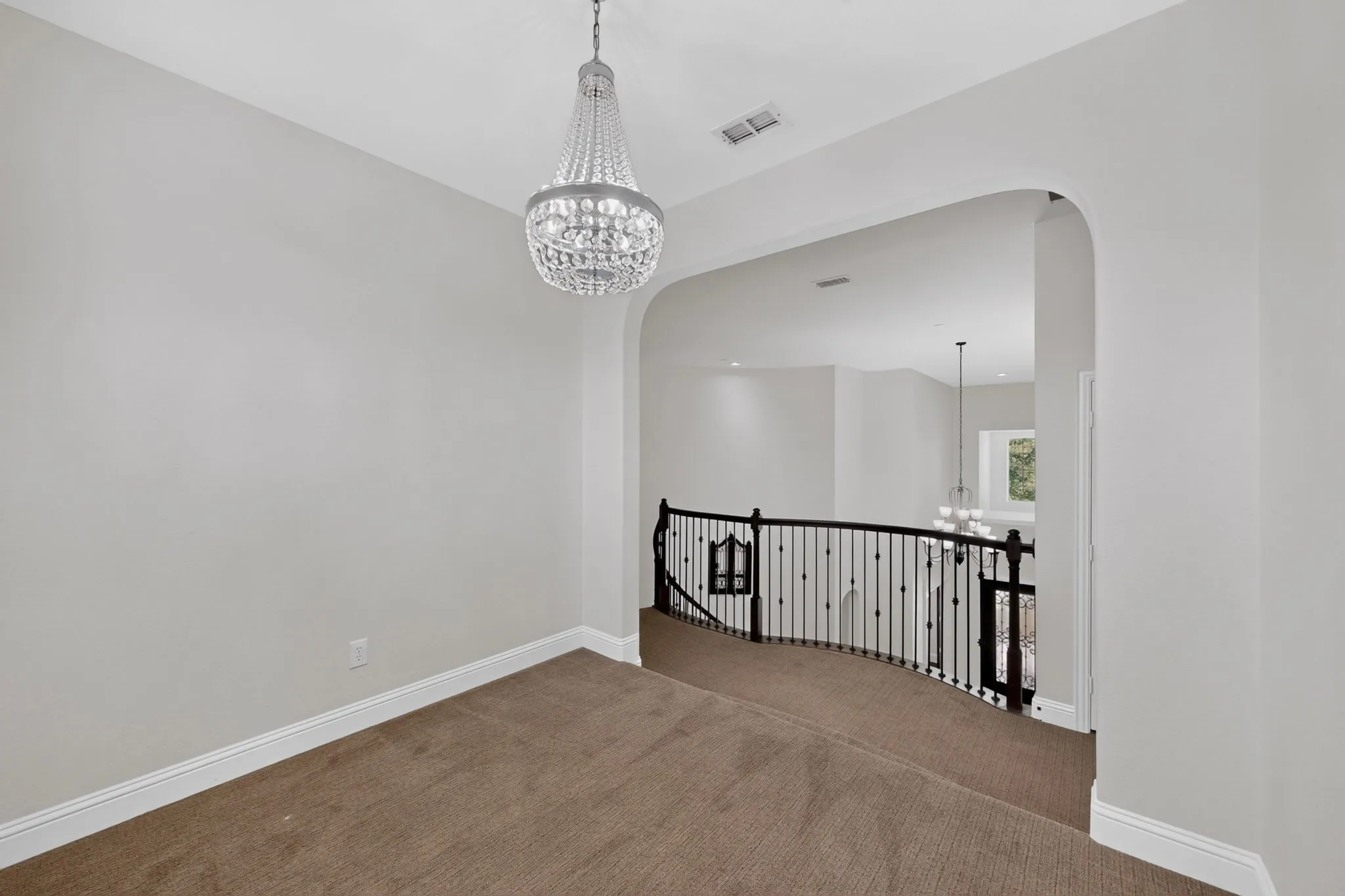 Upper-level landing featuring a crystal chandelier, arched entryway, and dark iron balusters
