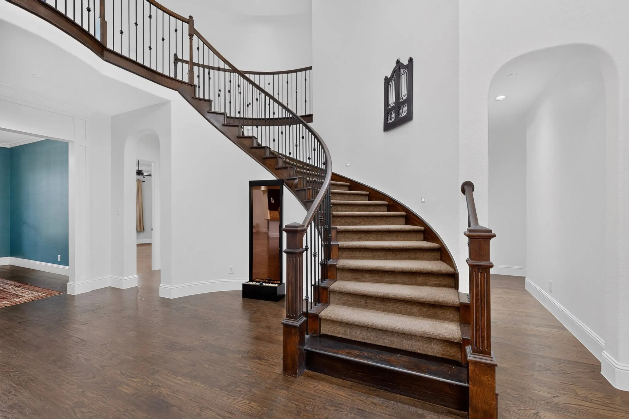 Grand curved staircase with dark wood-finish treads and risers, complemented by a wrought iron balustrade