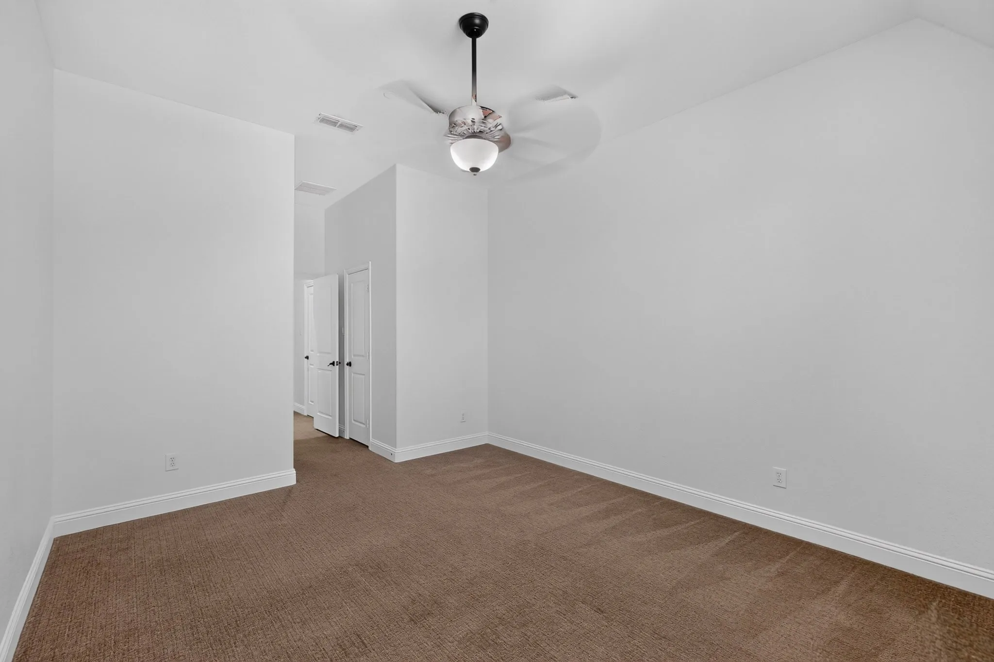 Spacious room featuring neutral carpeting, white walls, and a ceiling fan with integrated lighting