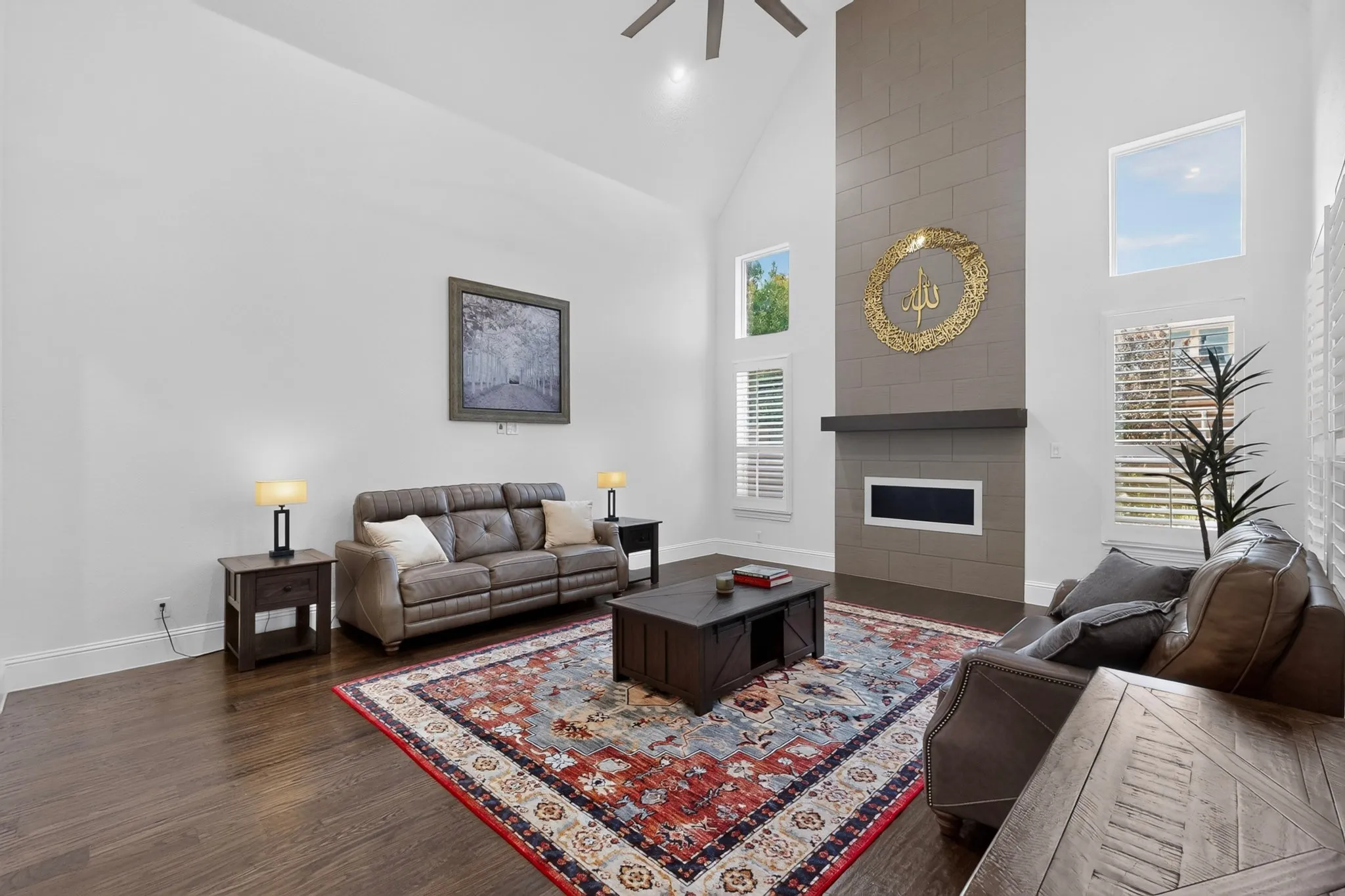 Living area featuring vaulted ceilings, wood-finish flooring, a contemporary fireplace with a stone surround, and multiple windows with plantation shutters