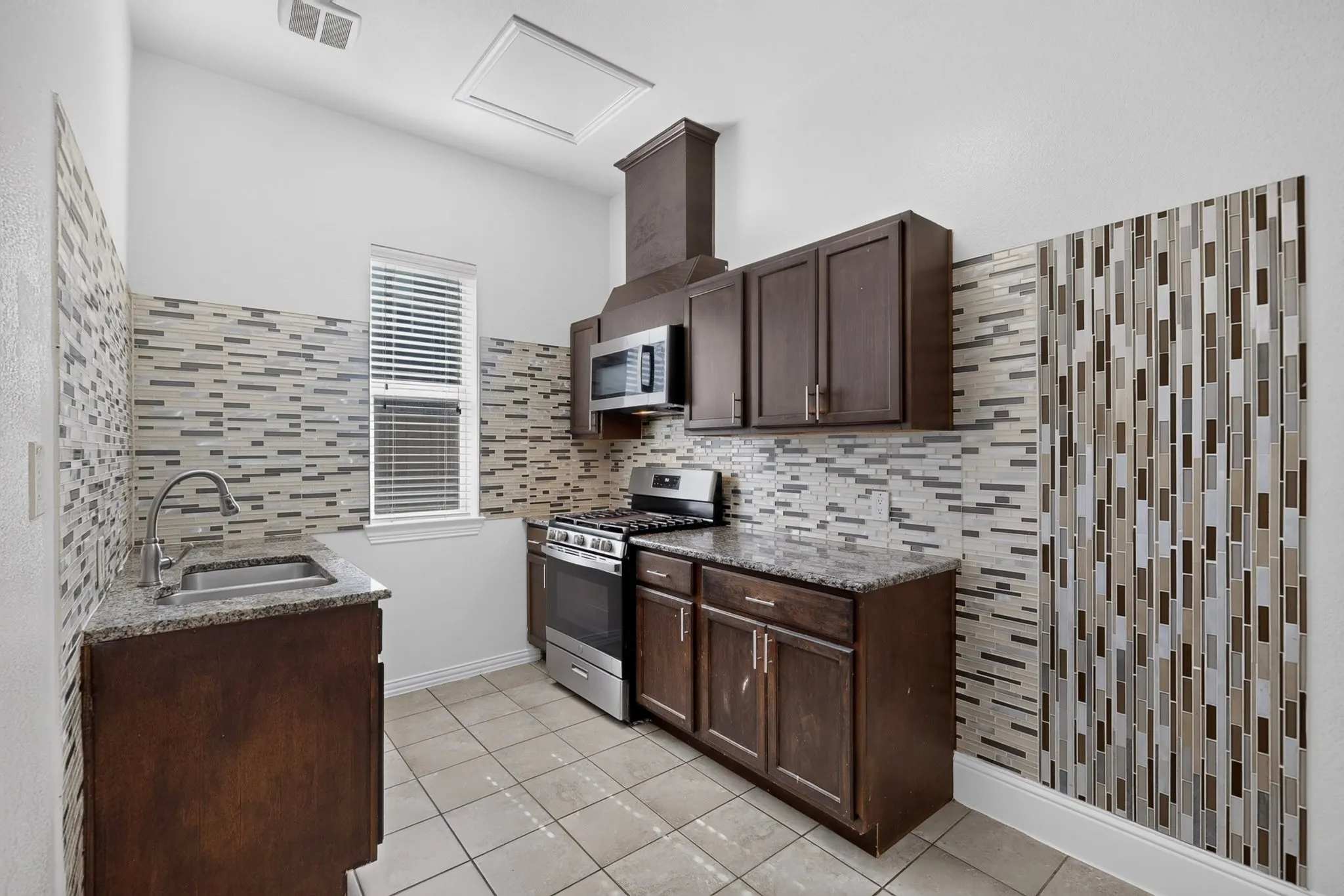 Kitchen featuring dark wood-finish cabinetry, granite-style countertops, stainless steel appliances, and a decorative tile backsplash