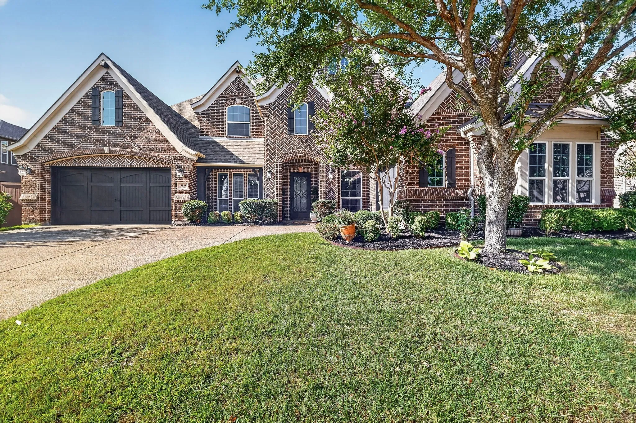 Brick facade residence featuring a two-car garage, mature landscaping, and an arched entry