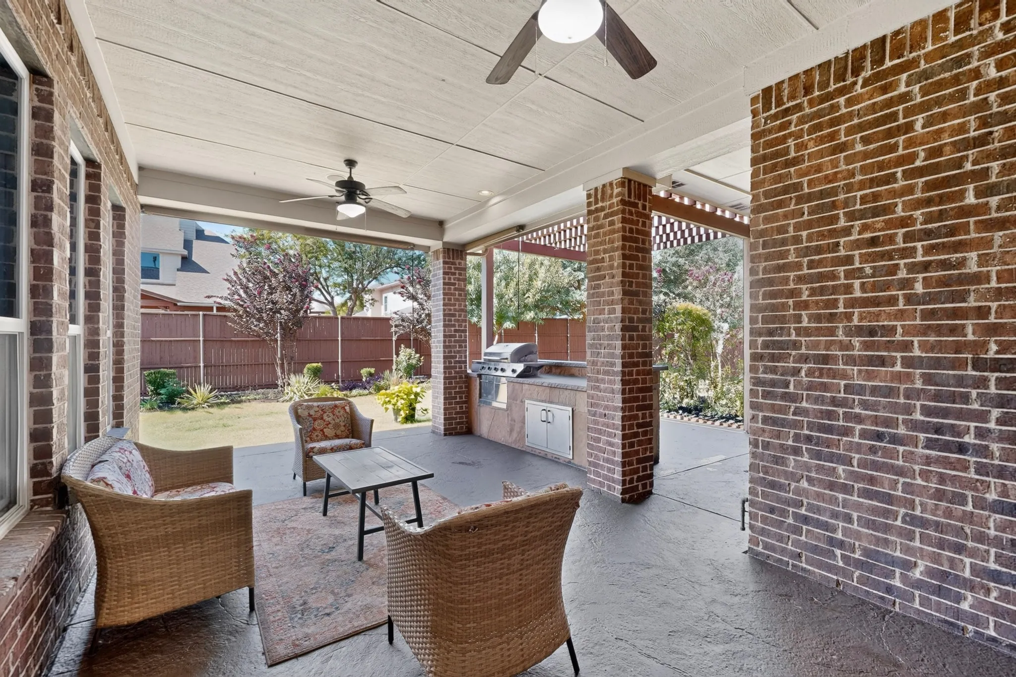 Covered patio featuring a built-in outdoor kitchen with a grill, brick columns, and a stamped concrete floor