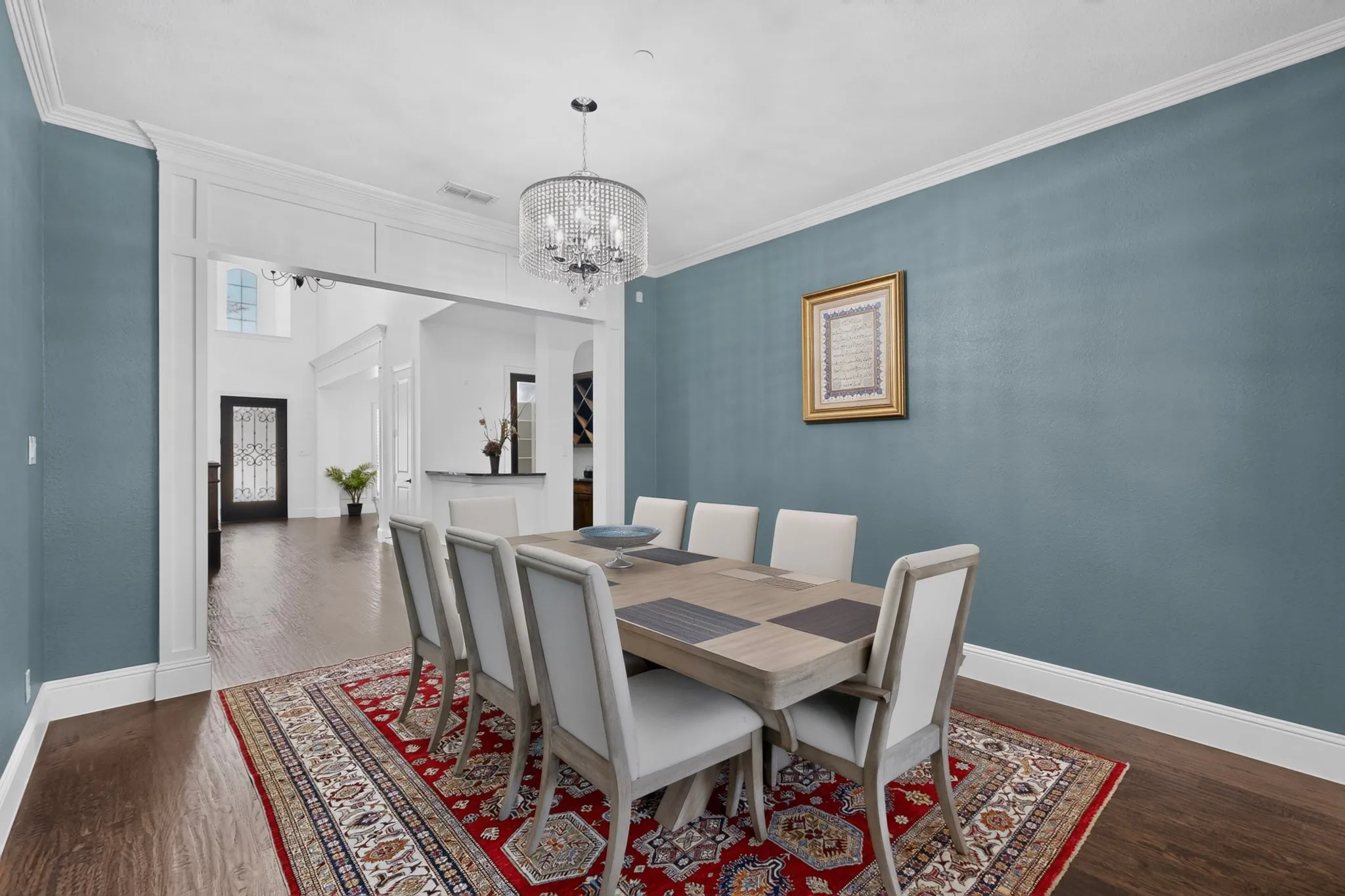 Spacious dining area featuring wood-finish flooring, a decorative chandelier, crown molding, and an arched entry