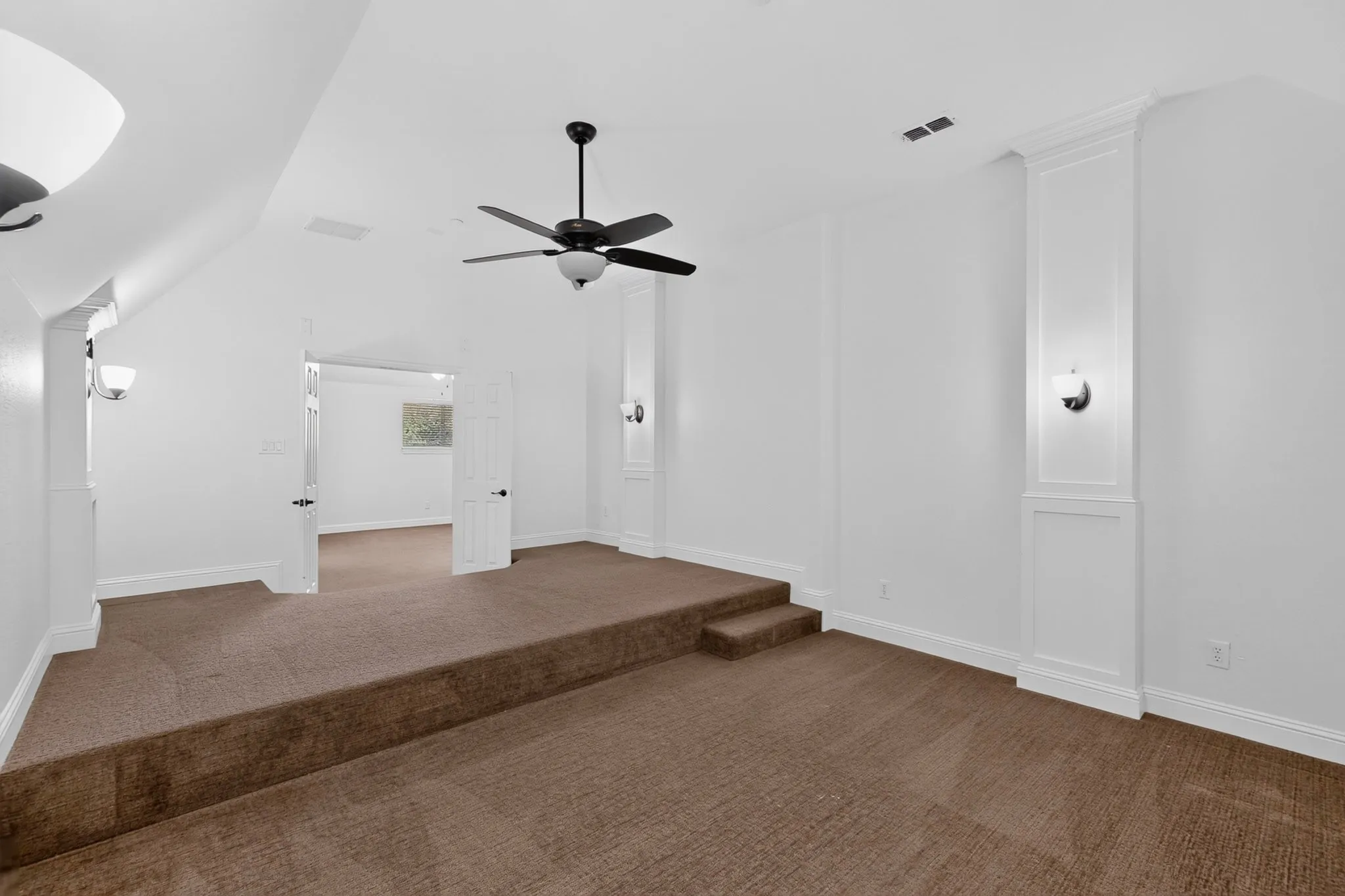 Carpeted multi-level room featuring a ceiling fan, wall sconces, and white trim molding