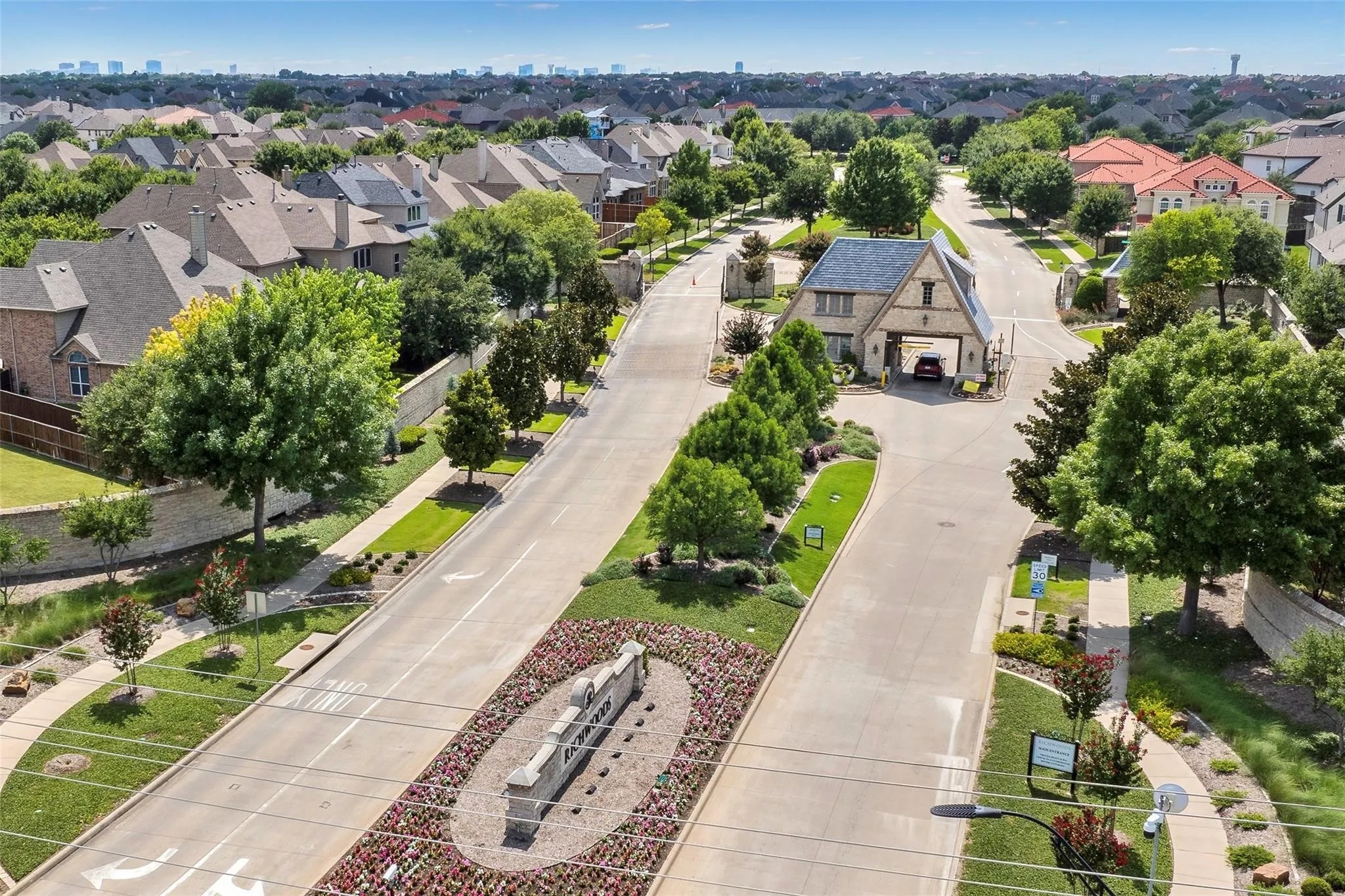 Gated community entrance featuring stone and timber-frame architecture, lush landscaping, and a manicured streetscape