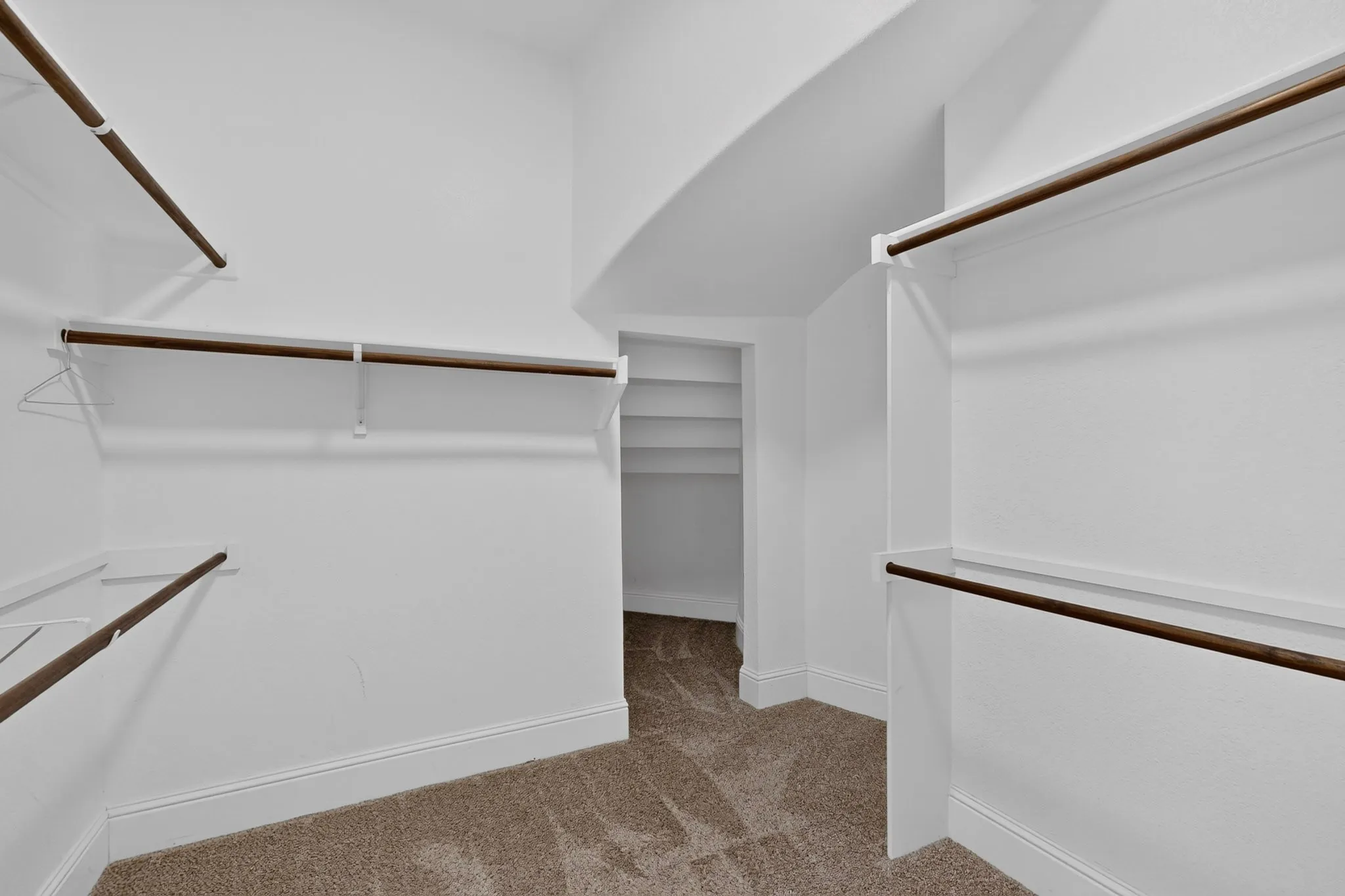 Spacious walk-in closet featuring multiple shelving units with hanging rods, white trim, and neutral carpet flooring
