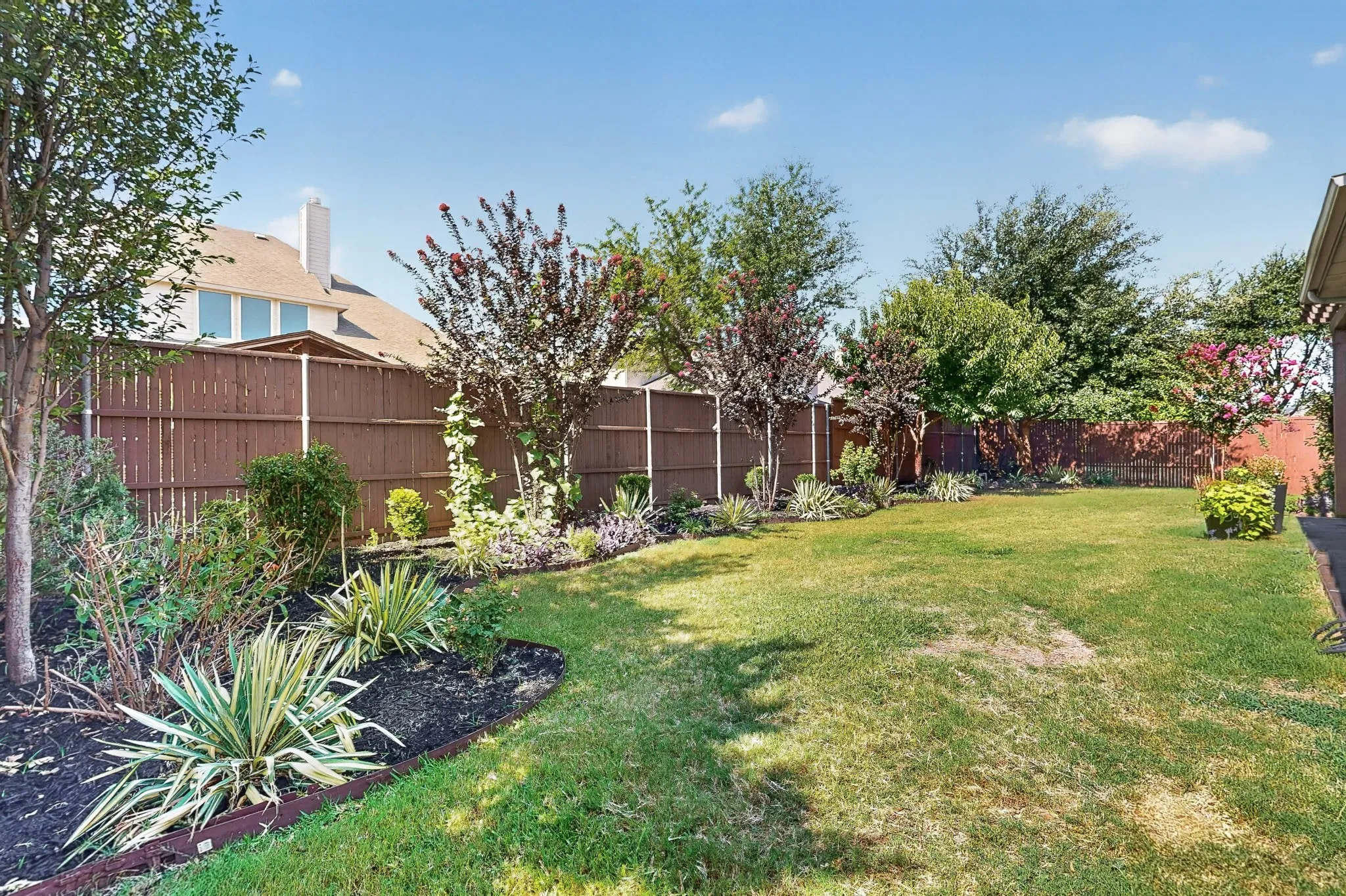 Spacious backyard with a vibrant green lawn, featuring mature trees and established landscaping beds