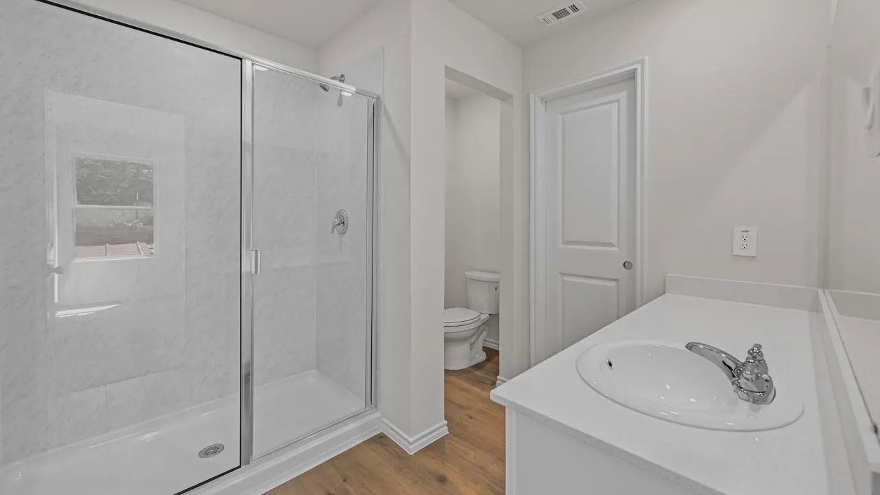 Modern bathroom featuring a glass-enclosed shower with white tiled walls, a white vanity with an integrated sink, chrome fixtures, and wood-finish flooring