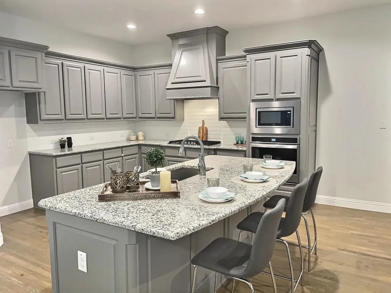 Kitchen featuring gray cabinetry, granite countertops, stainless steel appliances, a tile backsplash, and wood-finish flooring