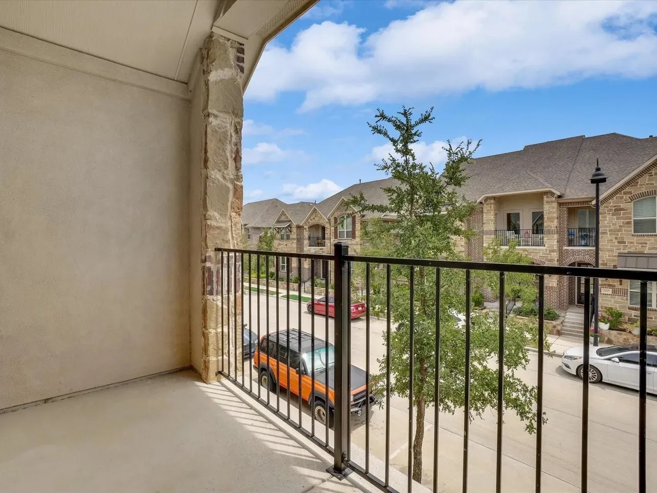 Private balcony with a decorative black metal railing, stucco wall, and stone column accents