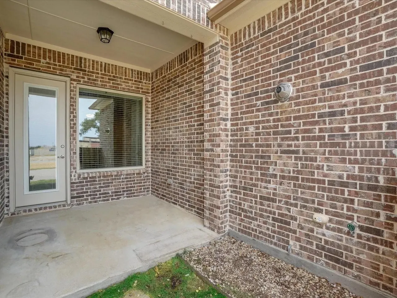 Covered patio featuring concrete flooring, brick exterior, and an exterior light fixture