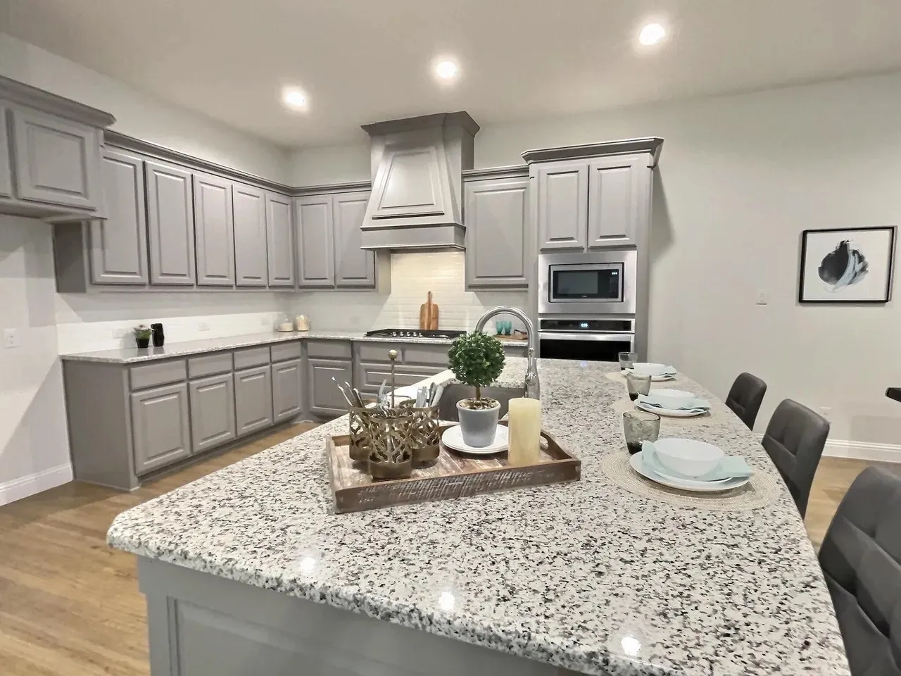 Kitchen featuring gray shaker-style cabinetry, a built-in microwave, a large kitchen island with counter seating, granite countertops, and wood-finish flooring