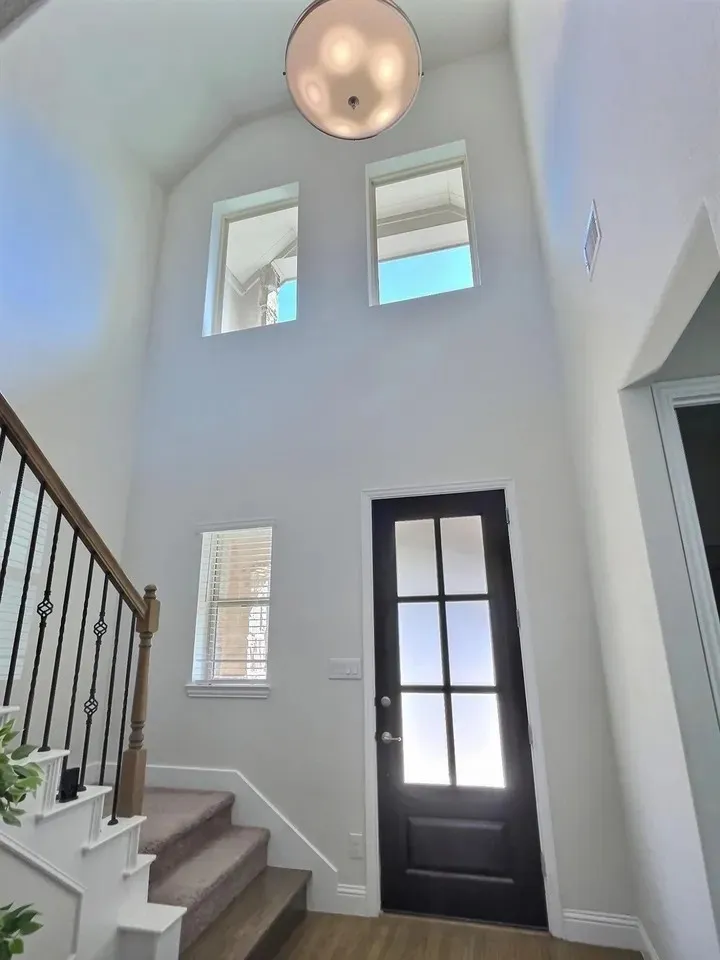 Two-story entry with a vaulted ceiling, prominent ceiling-mounted light fixture, dark-paneled door with glass inserts, and a staircase featuring wrought iron balusters