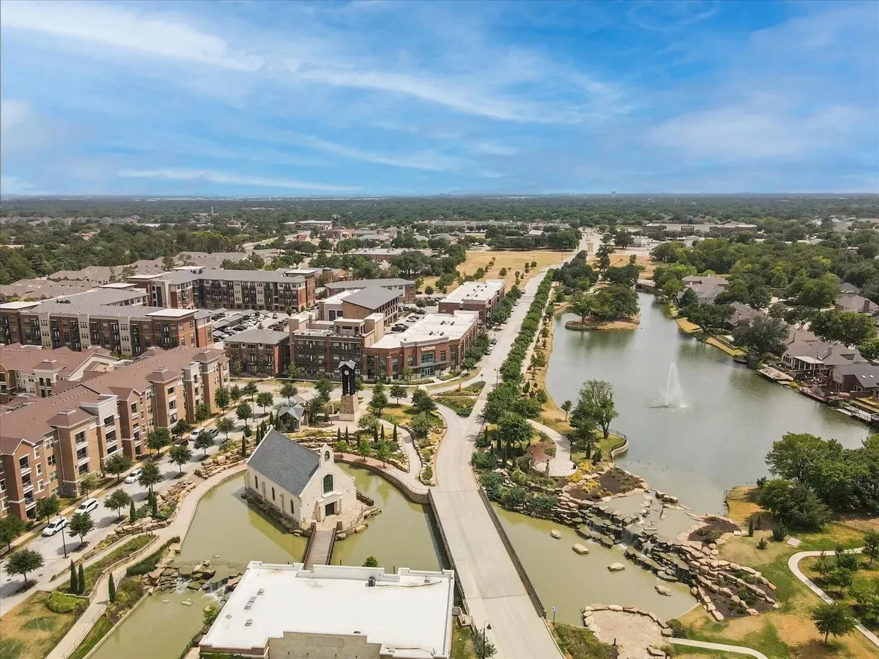 Aerial perspective of a mixed-use development featuring multi-story residential buildings, commercial structures, and a prominent water feature with a fountain