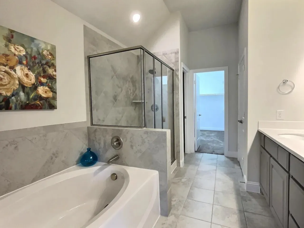 Built-in tub with a tiled surround, glass-enclosed shower with tile, and dual vanity with white countertops and gray cabinetry